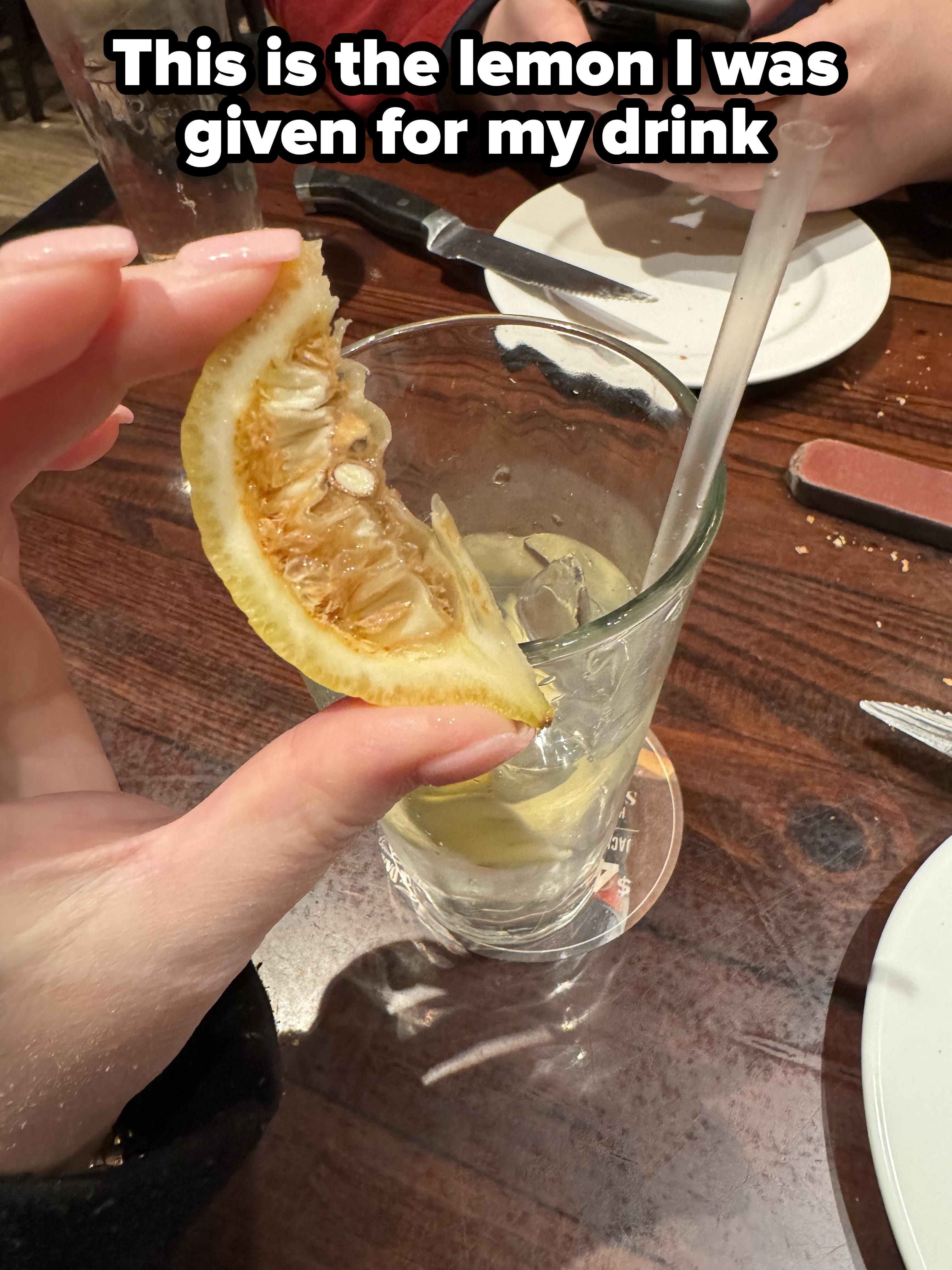 A person holds a desiccated, old lemon slice with caption &quot;This is the lemon I was given for my drink&quot;