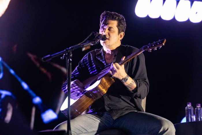 John Mayer playing guitar on stage while singing