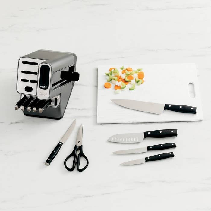the knife set with knives laid out on a cutting board next to veggies