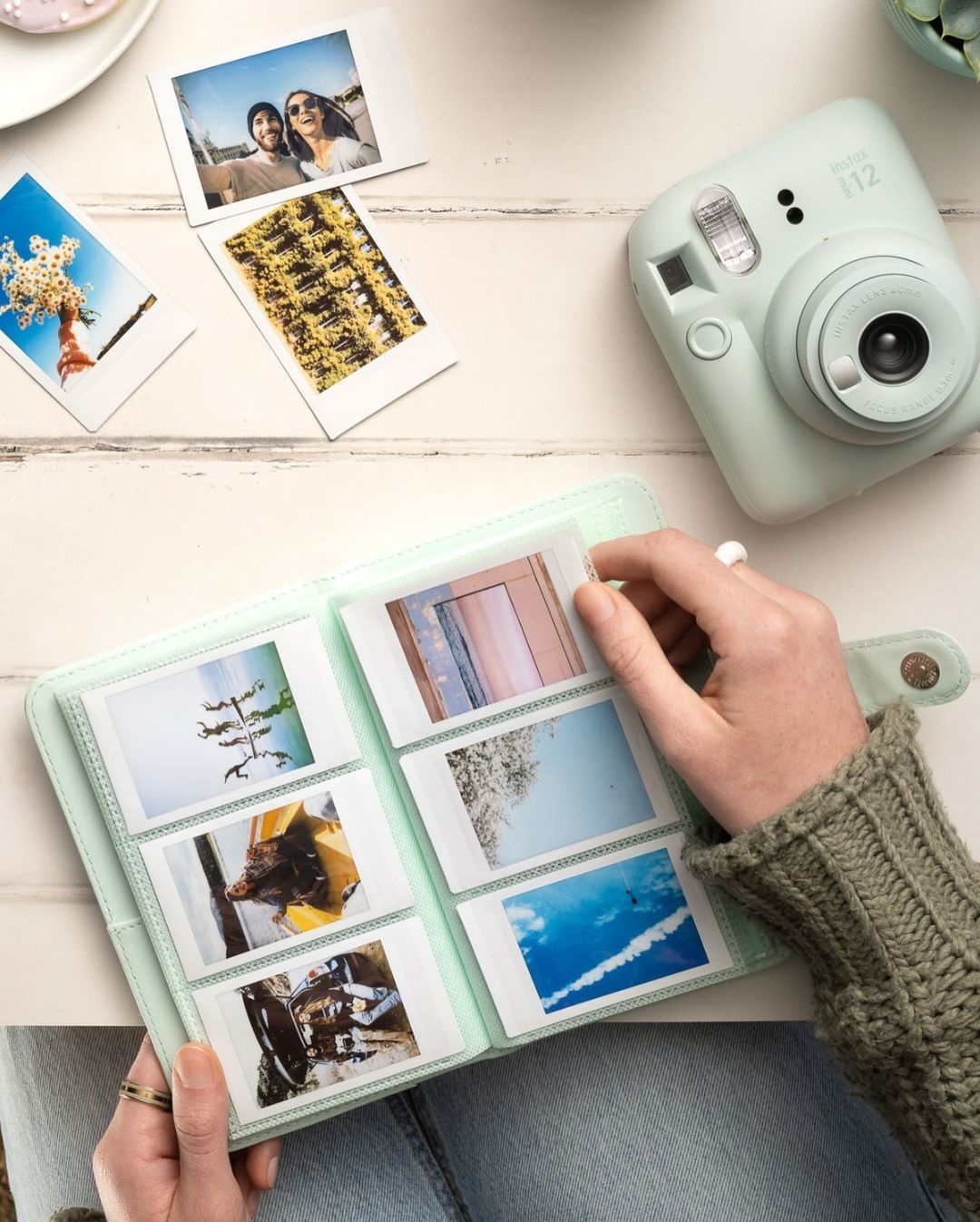 the instax camera in the color mint green displayed with a photo album