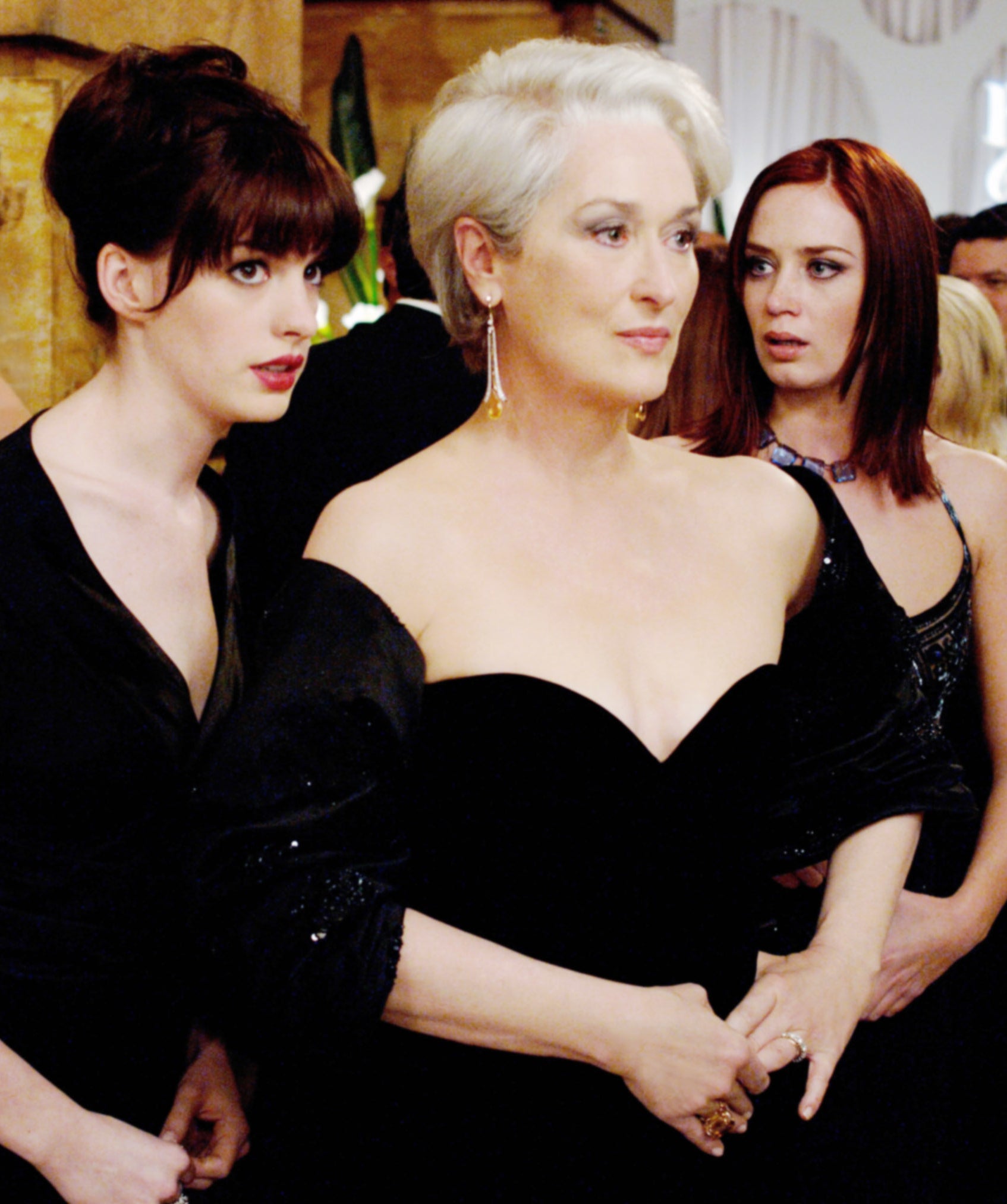 Anne Hathaway and Emily Blunt stand behind Meryl at a formal event in a scene from &quot;The Devil Wears Prada&quot;
