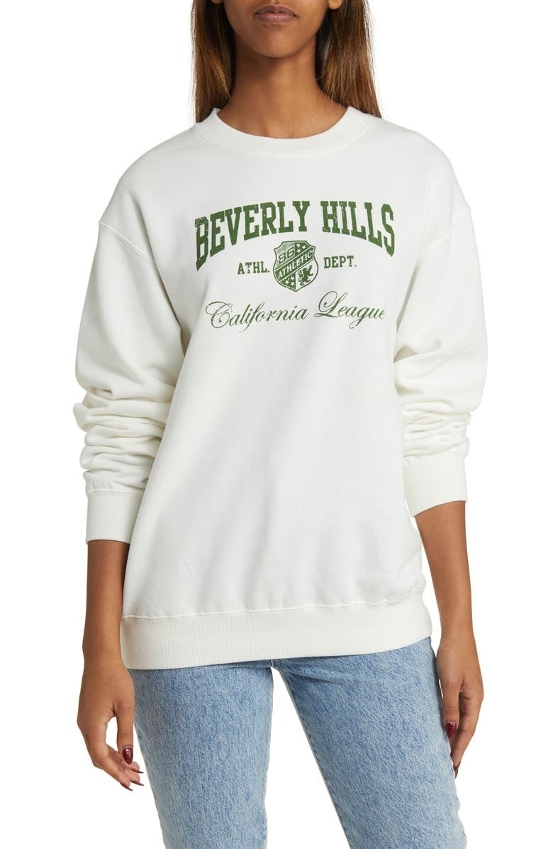 model wearing white sweatshirt with green letters that say &quot;Beverly Hills&quot; on front