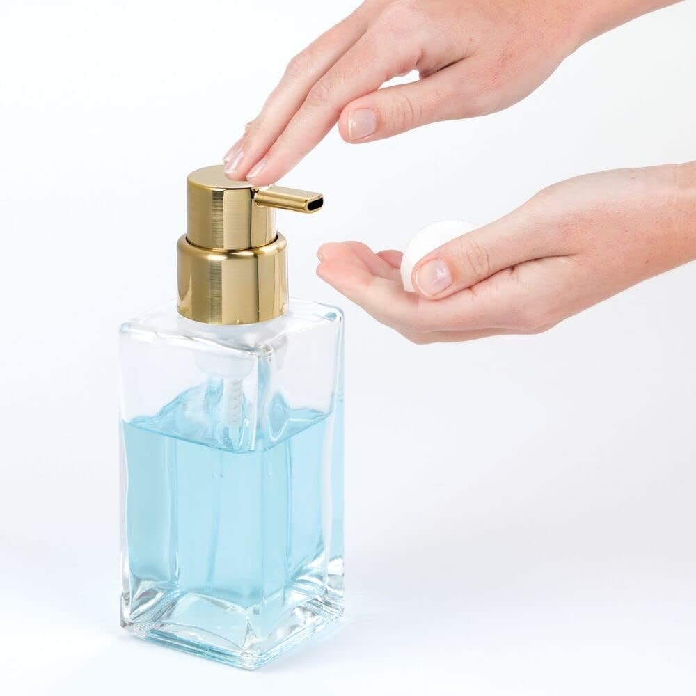 models hands pumping foaming soap from gold pump with glass body