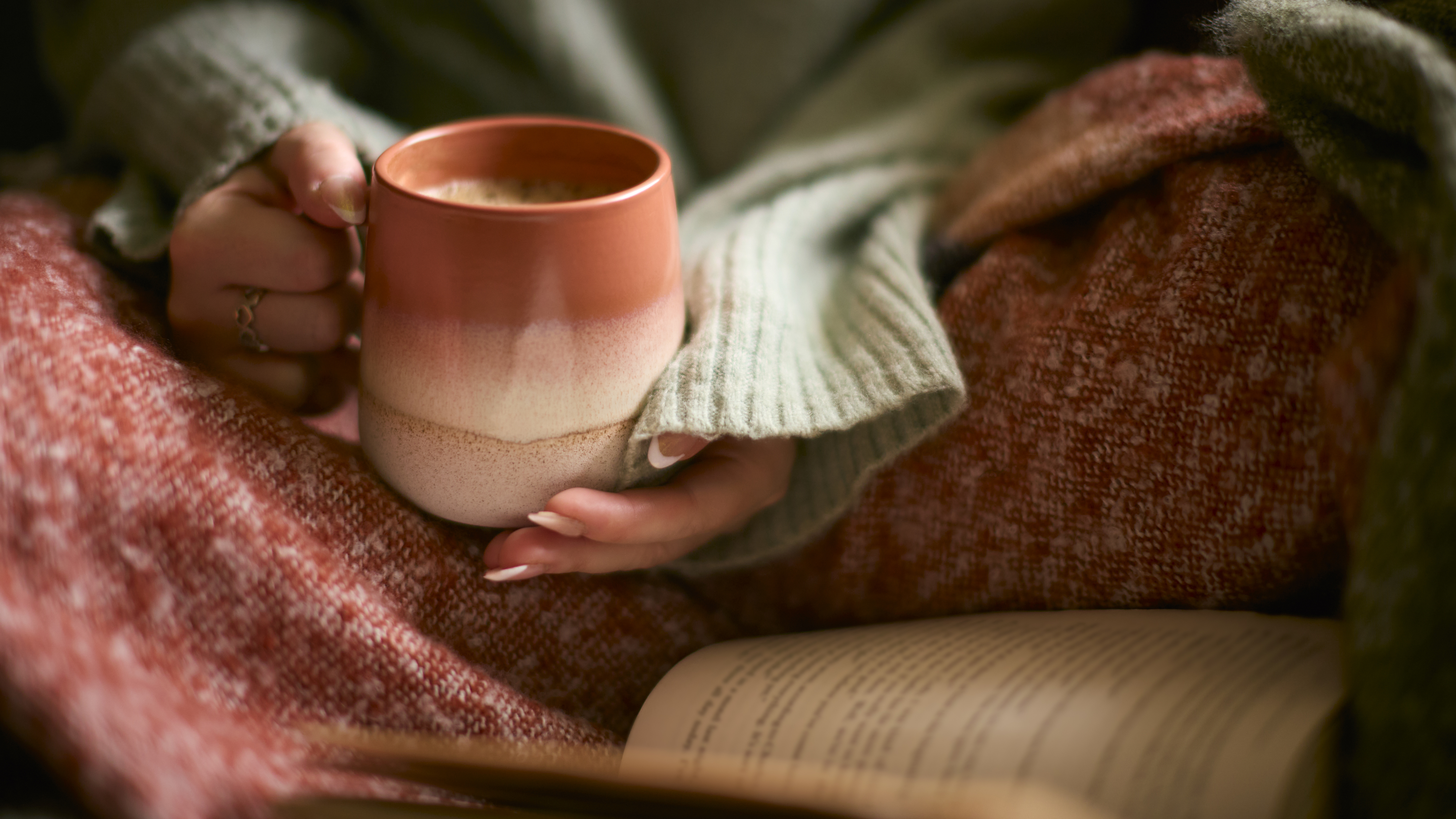 a person cozy on the couch with a mug and a book