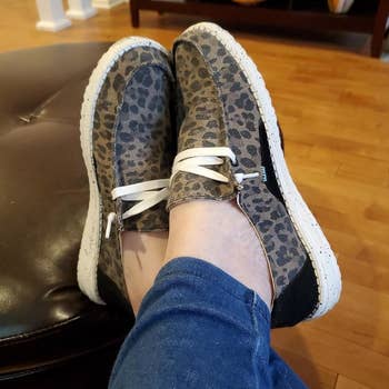 a reviewer wearing the slip-on shoes that feature white laces and an animal print