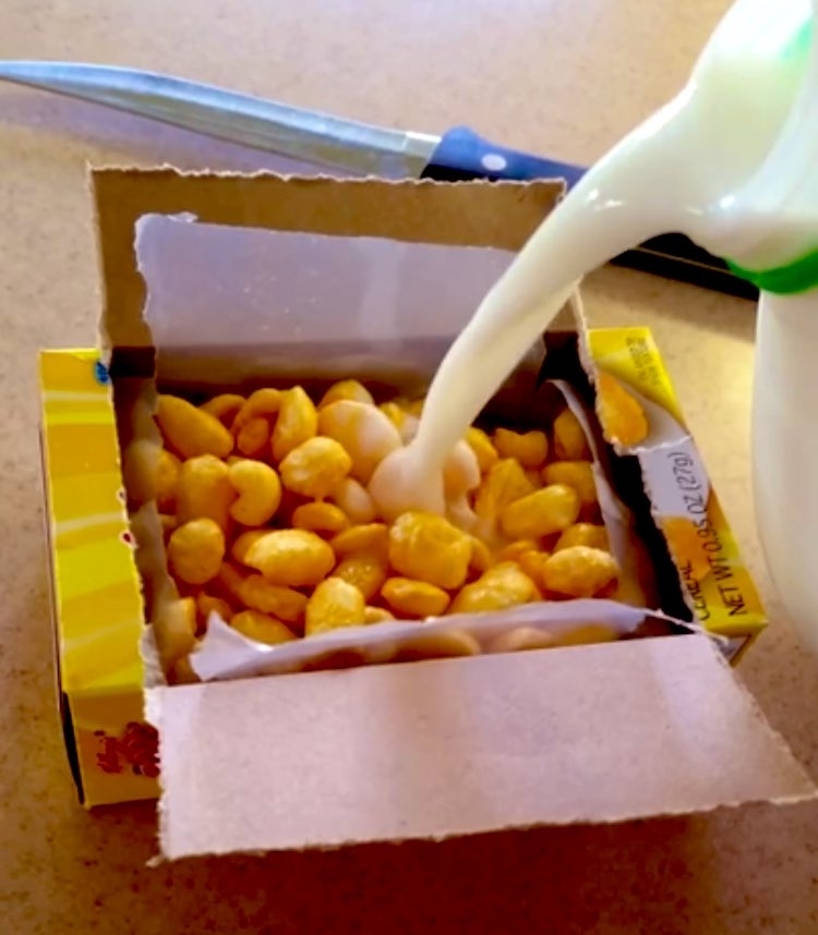 An open individual-serving cereal box and someone pouring milk into it