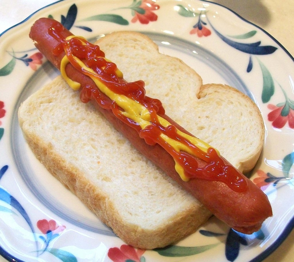 A hot dog with mustard and ketchup on a slice of white bread