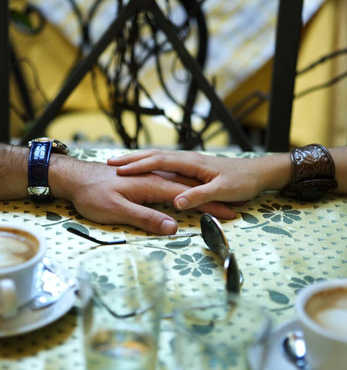 Woman&#x27;s hand on top of man&#x27;s hand on table in a café