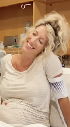 Emily in striped shirt smiling with her eyes closed, sitting in a hospital bed