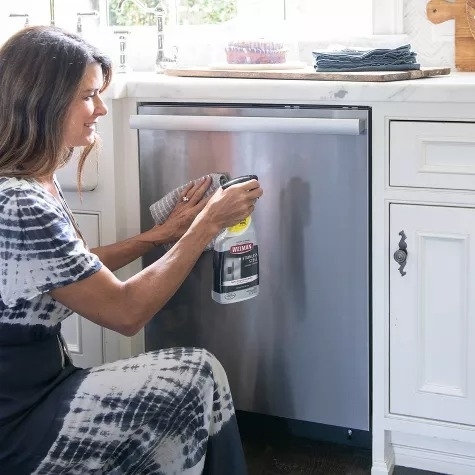 A person uses a stainless steel cleaner on a dishwasher