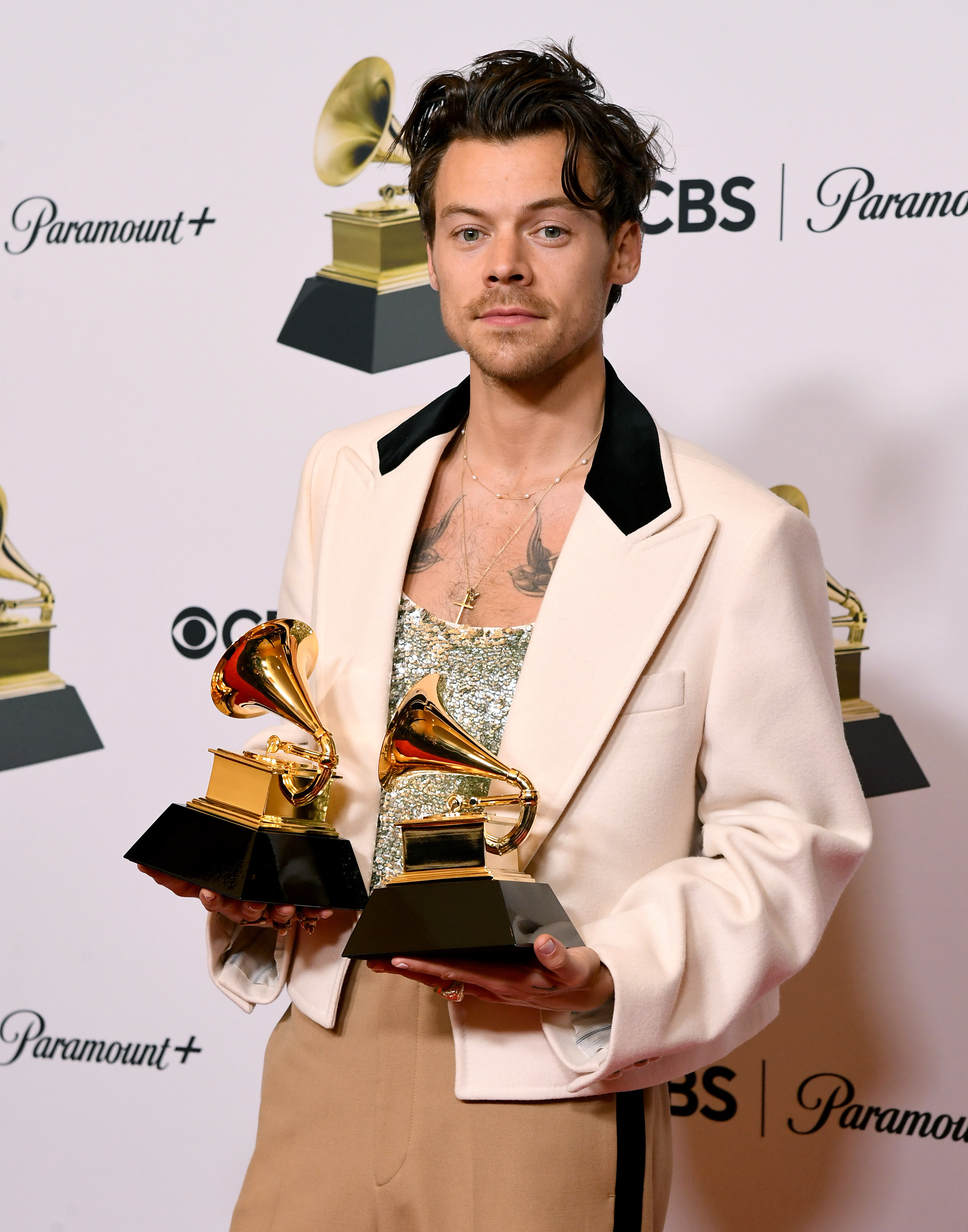 his chest tattoos are showing above his shirt and he&#x27;s holding two awards