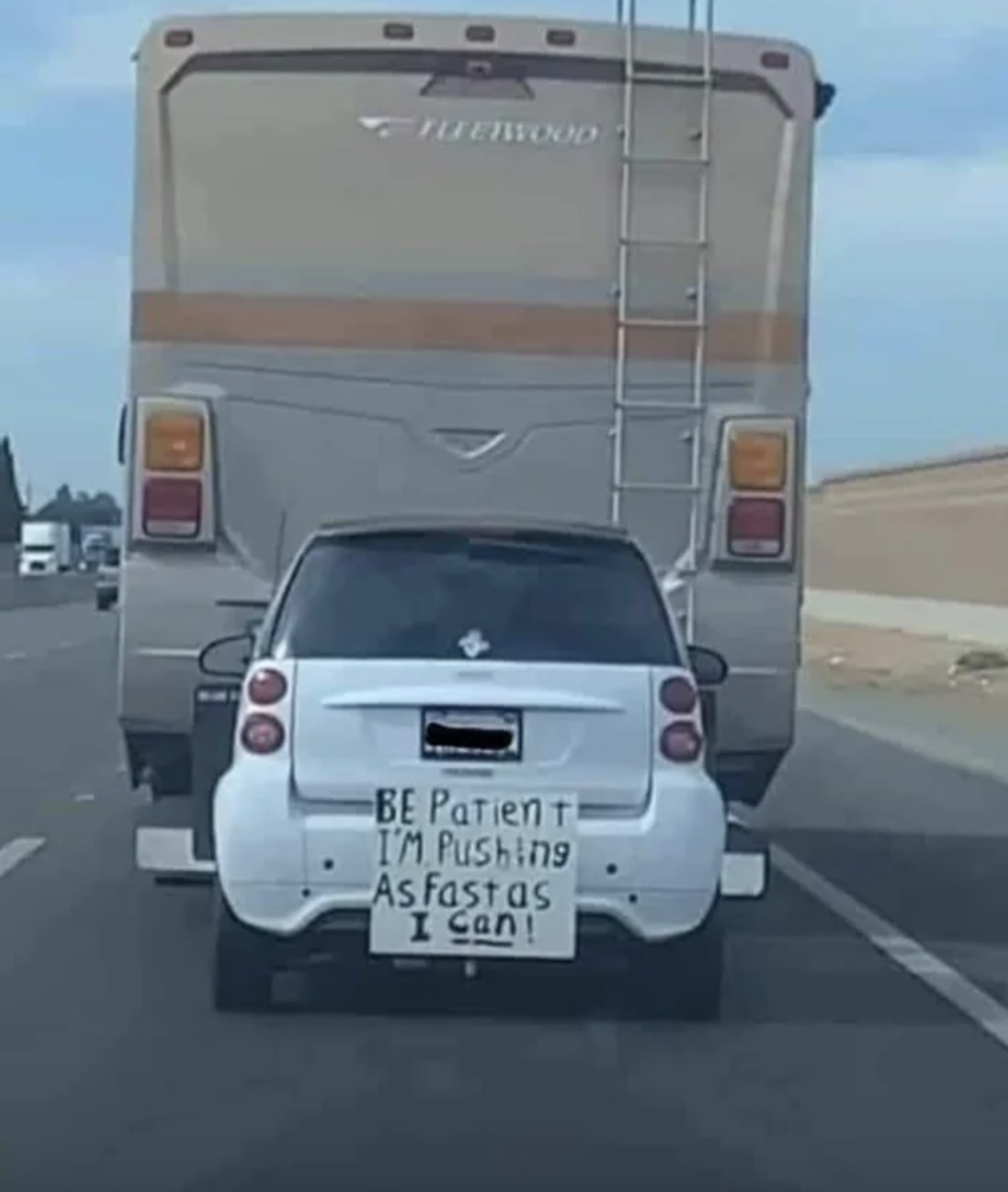 Sign on the back of a little car behind large trailer: &quot;Be patient I&#x27;m pushing as fast as I can!&quot;