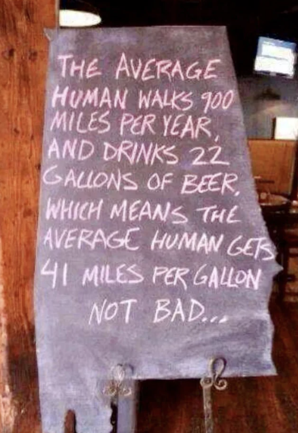 Handwritten sign: &quot;The average human walks 900 miles per year and drinks 22 gallons of beer, which means the average human gets 41 miles per gallon, not bad&quot;