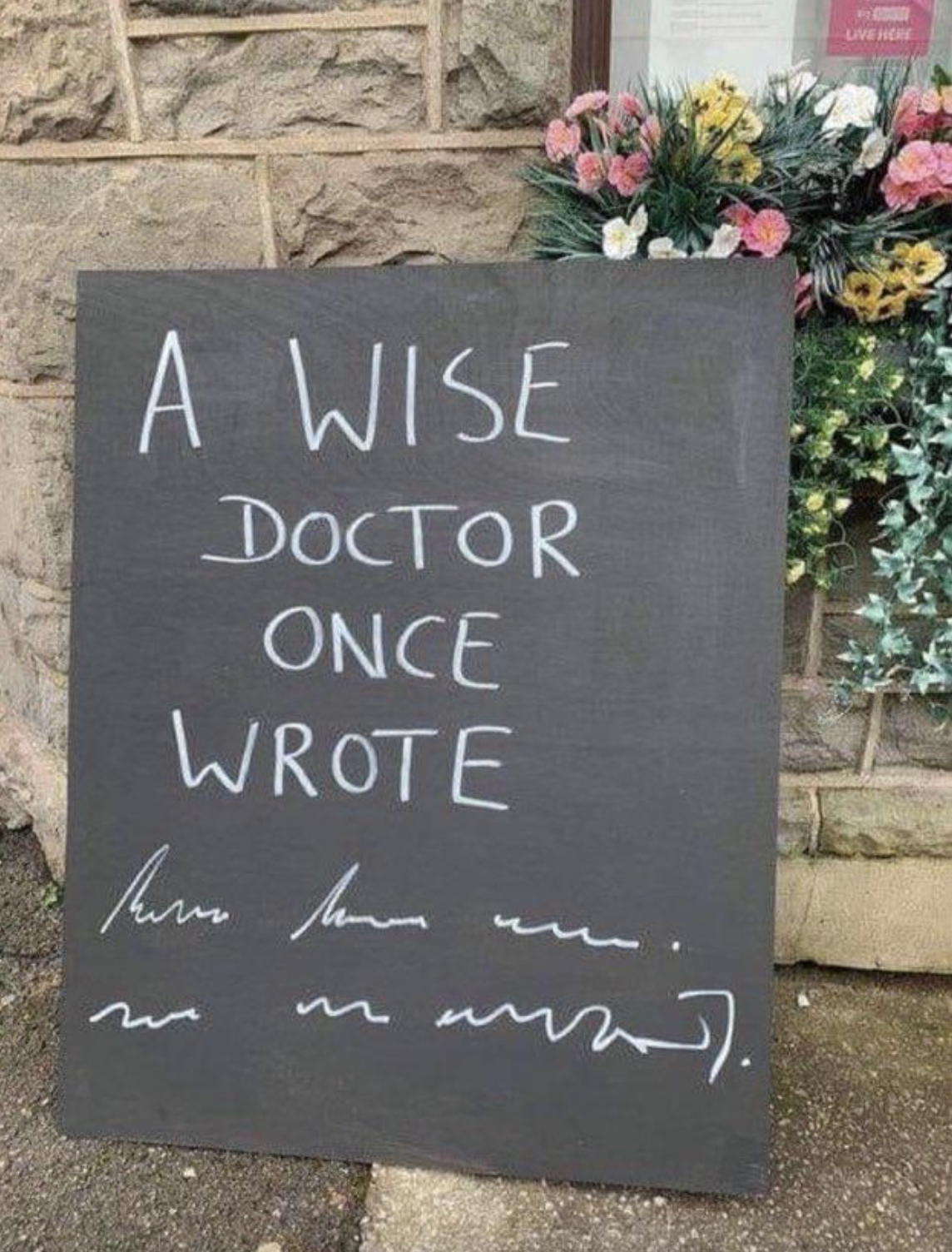 Handwritten sign on chalkboard: &quot;A wise doctor once wrote&quot; followed by an indecipherable scrawl