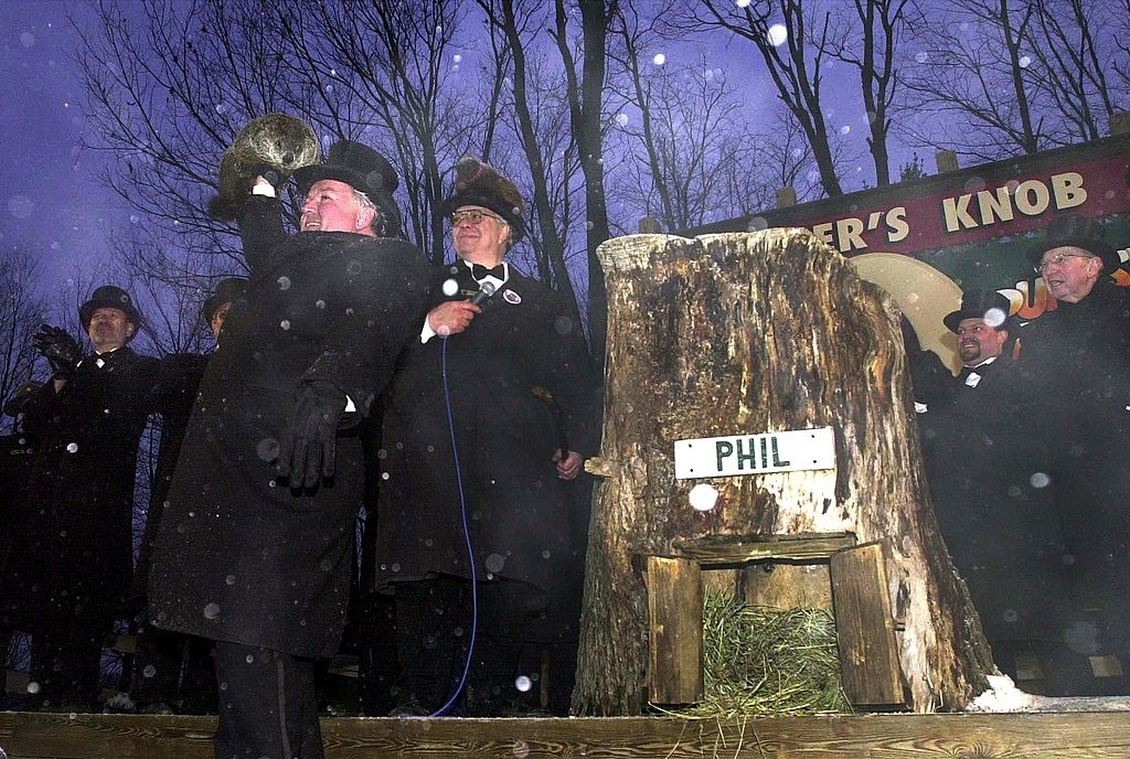 people outside while it snows standing next to a stump with the name tag of Phil