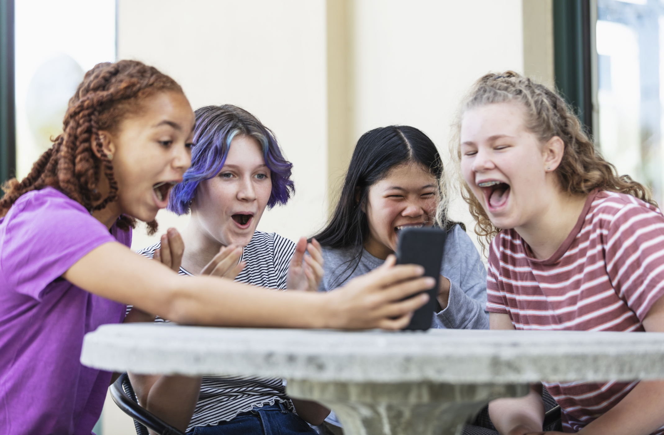 Teens laughing together at a table while looking at a phone