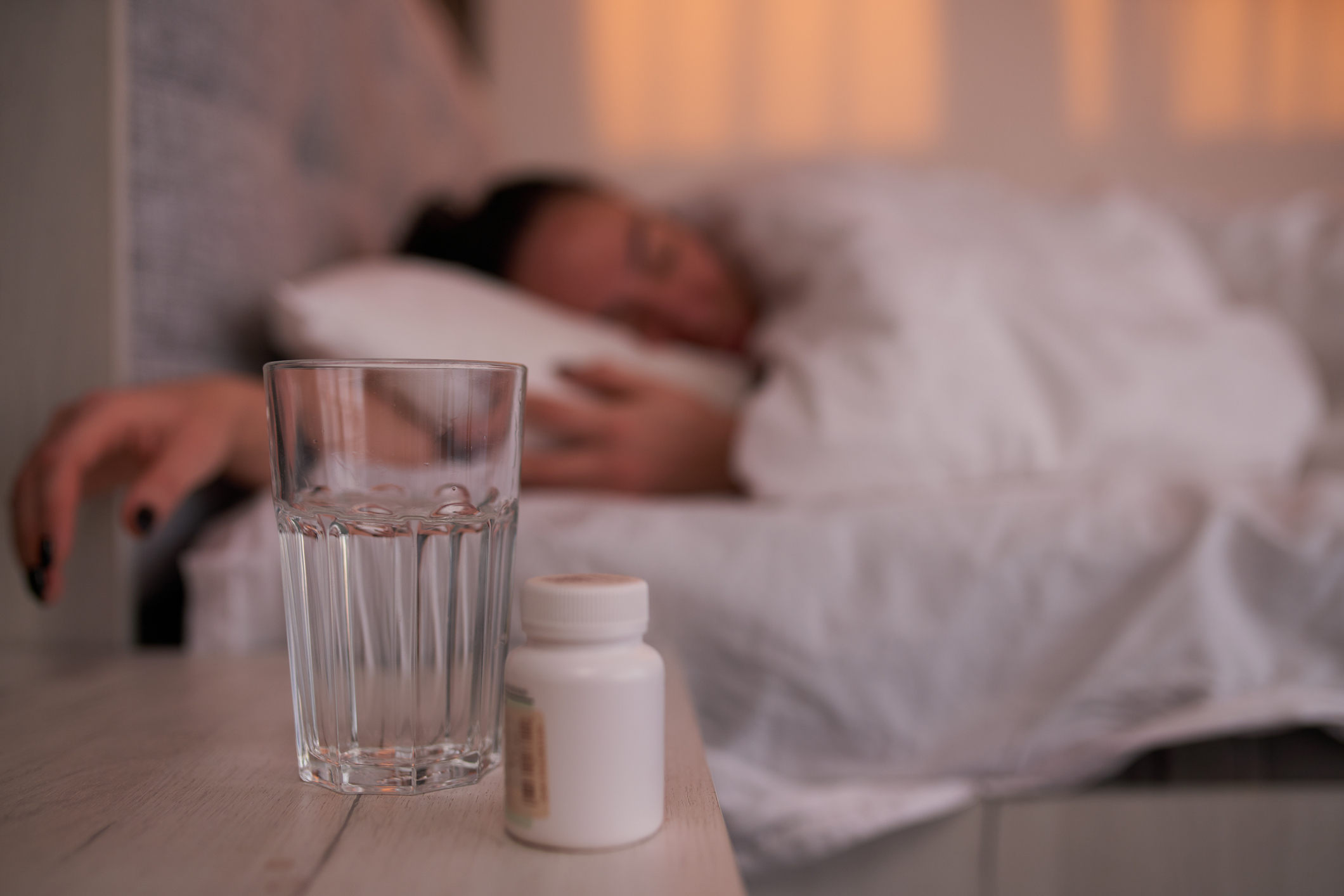 A person sleeping in bed with a glass of water and a pill bottle on the night table