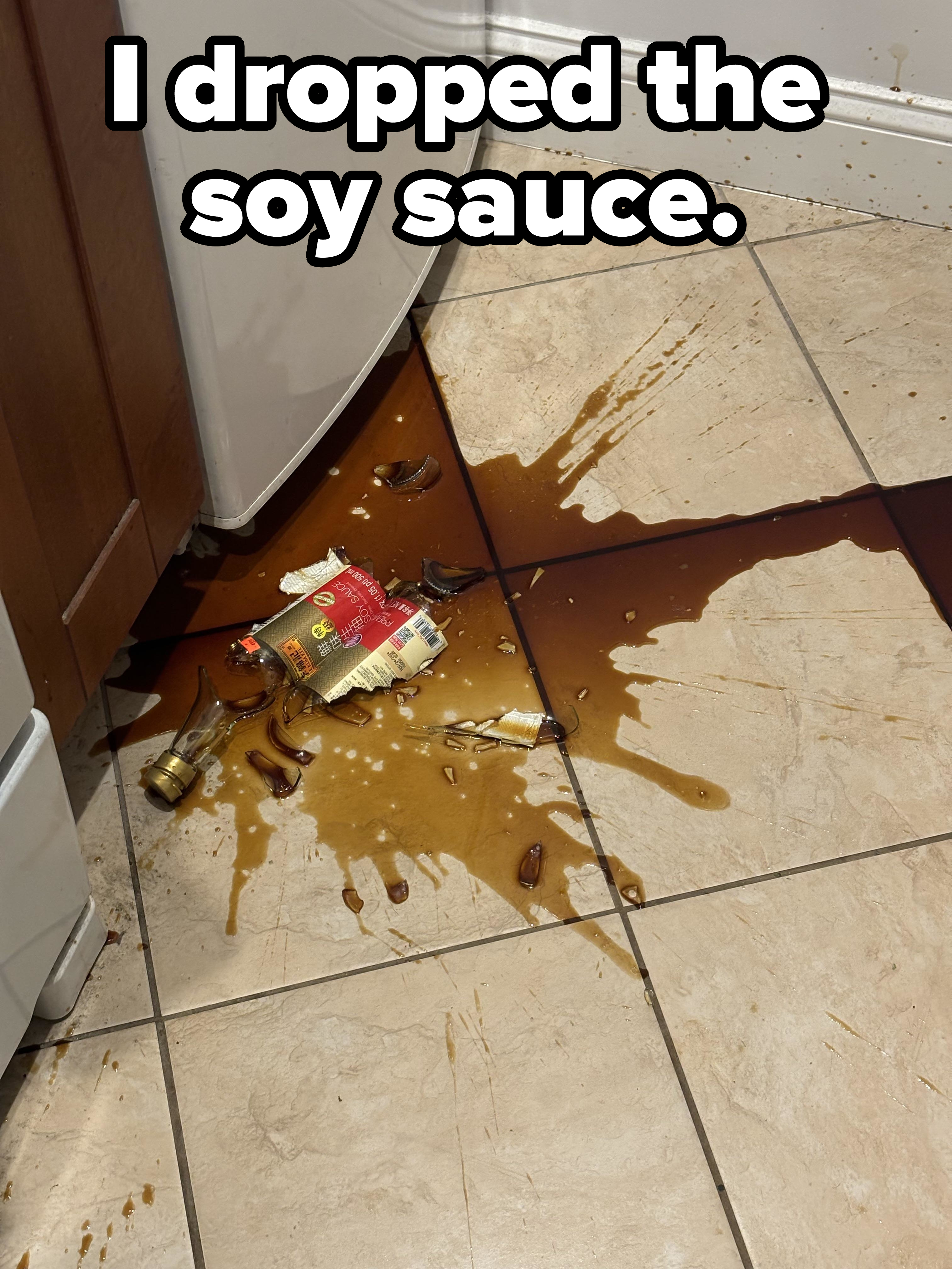 A broken bottle of soy sauce and its contents all over a kitchen floor