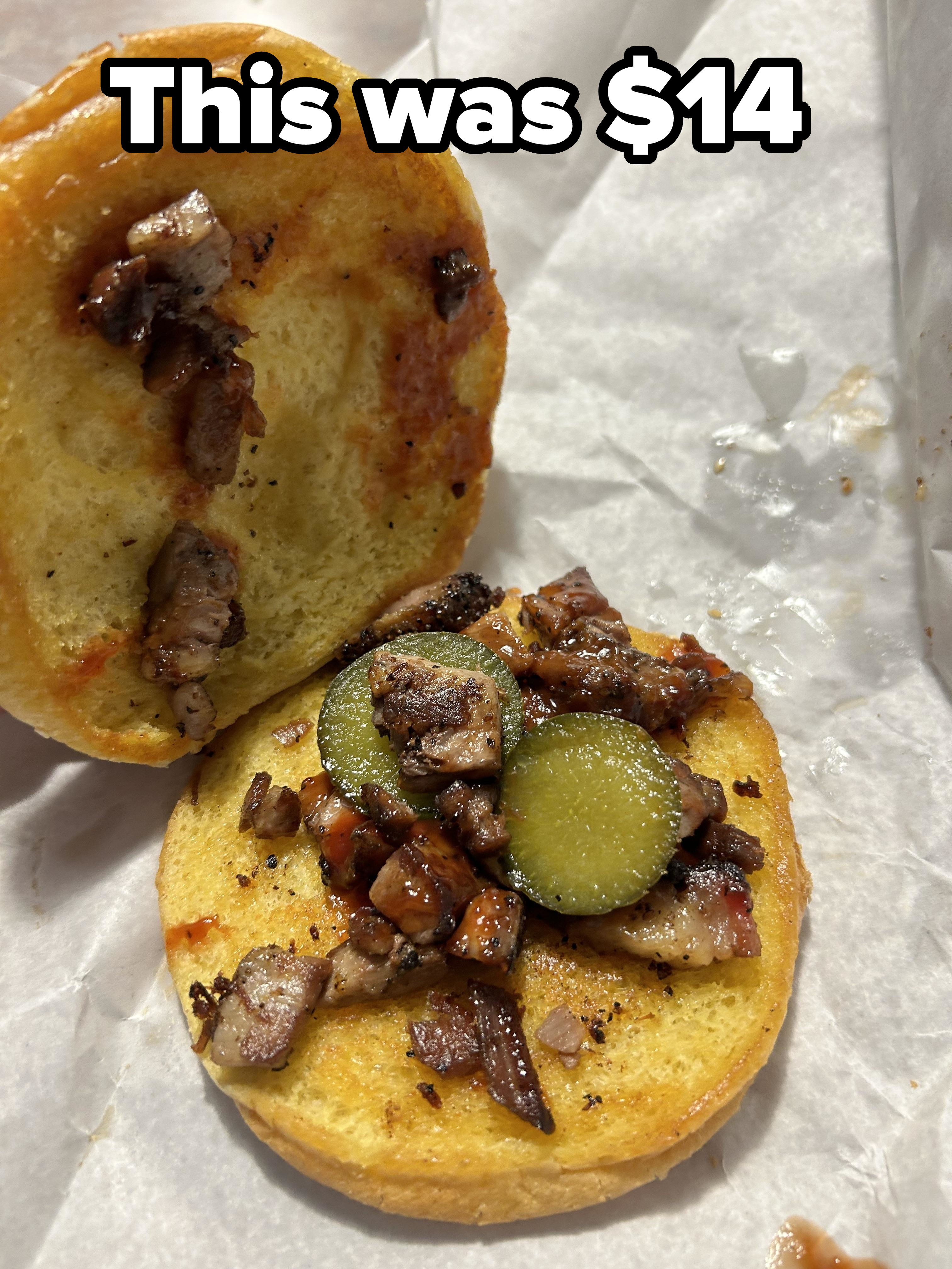 A $14 sandwich that consists of a bun, scant small pieces of meat, and two sad pickle slices