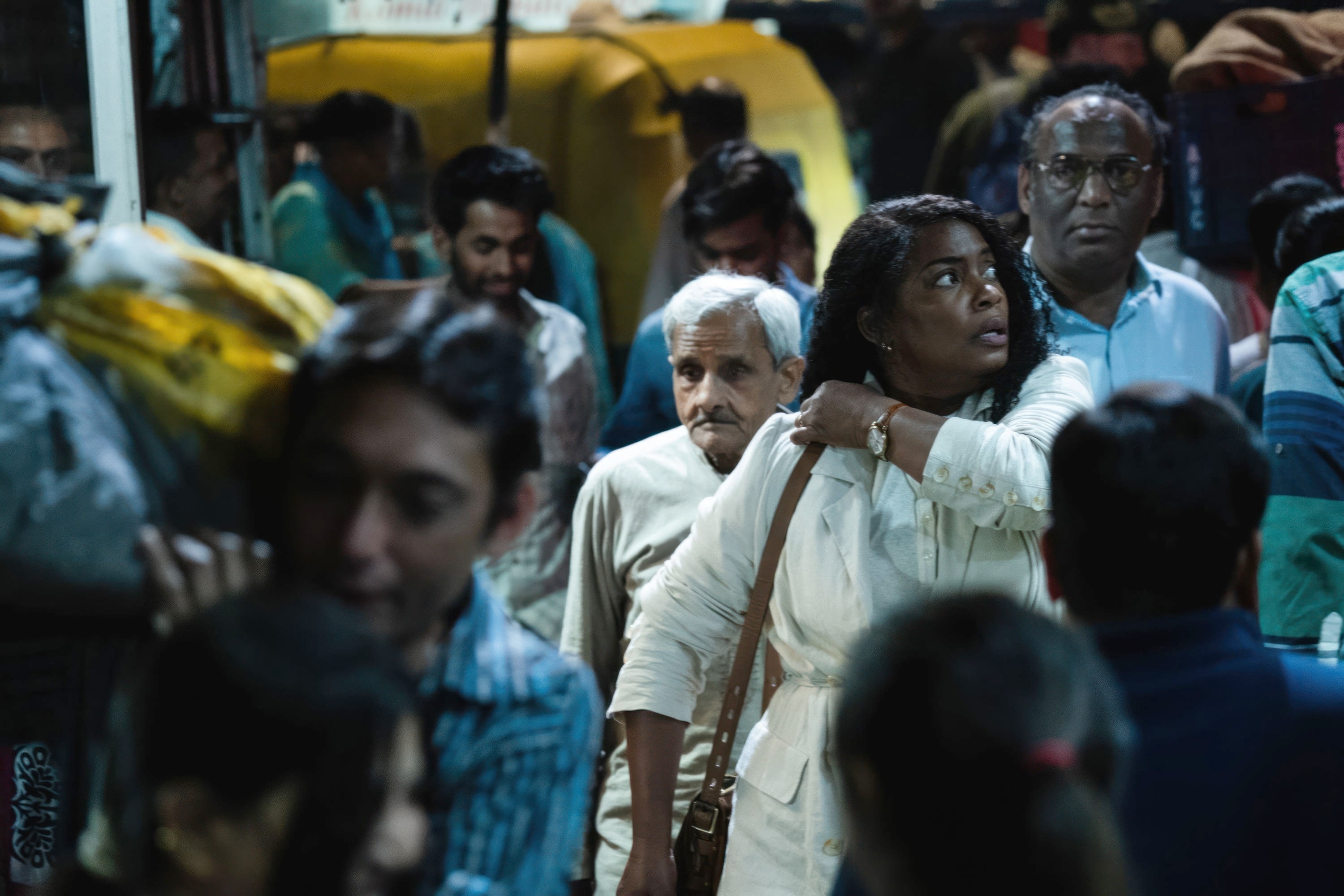 Aunjanue Ellis-Taylor in the foreground looking back in a crowded street scene, with onlookers and a tuk-tuk in the background in a scene from &quot;Origin&quot;