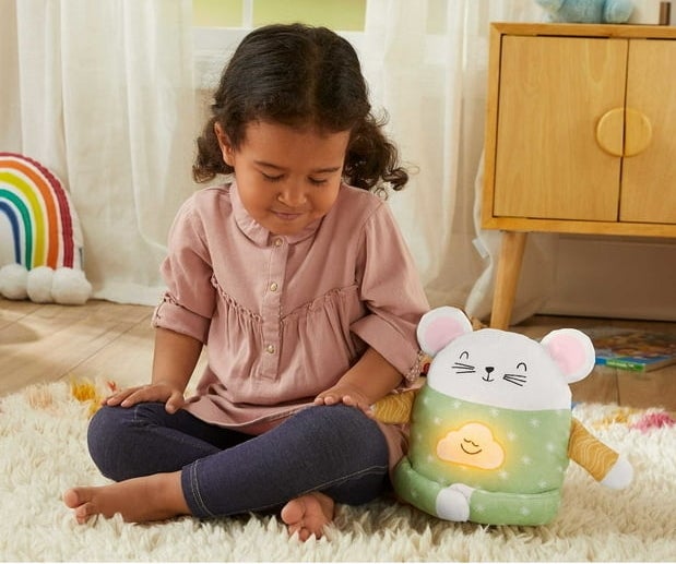a child sitting cross legged with eyes closed next to the plush mouse