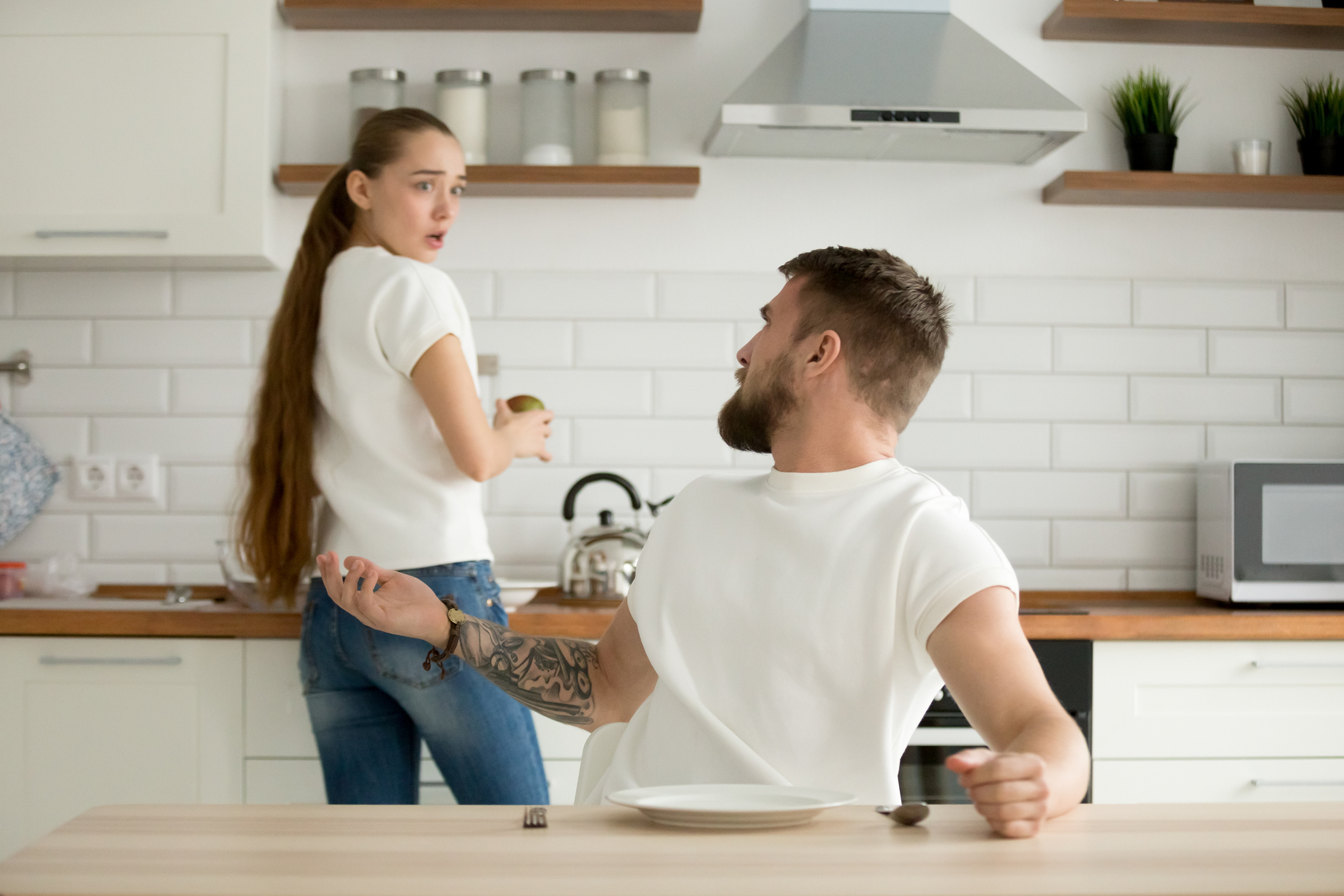 couple in kitchen, woman is at stove with a shocked look while man turns around and shrugs at her