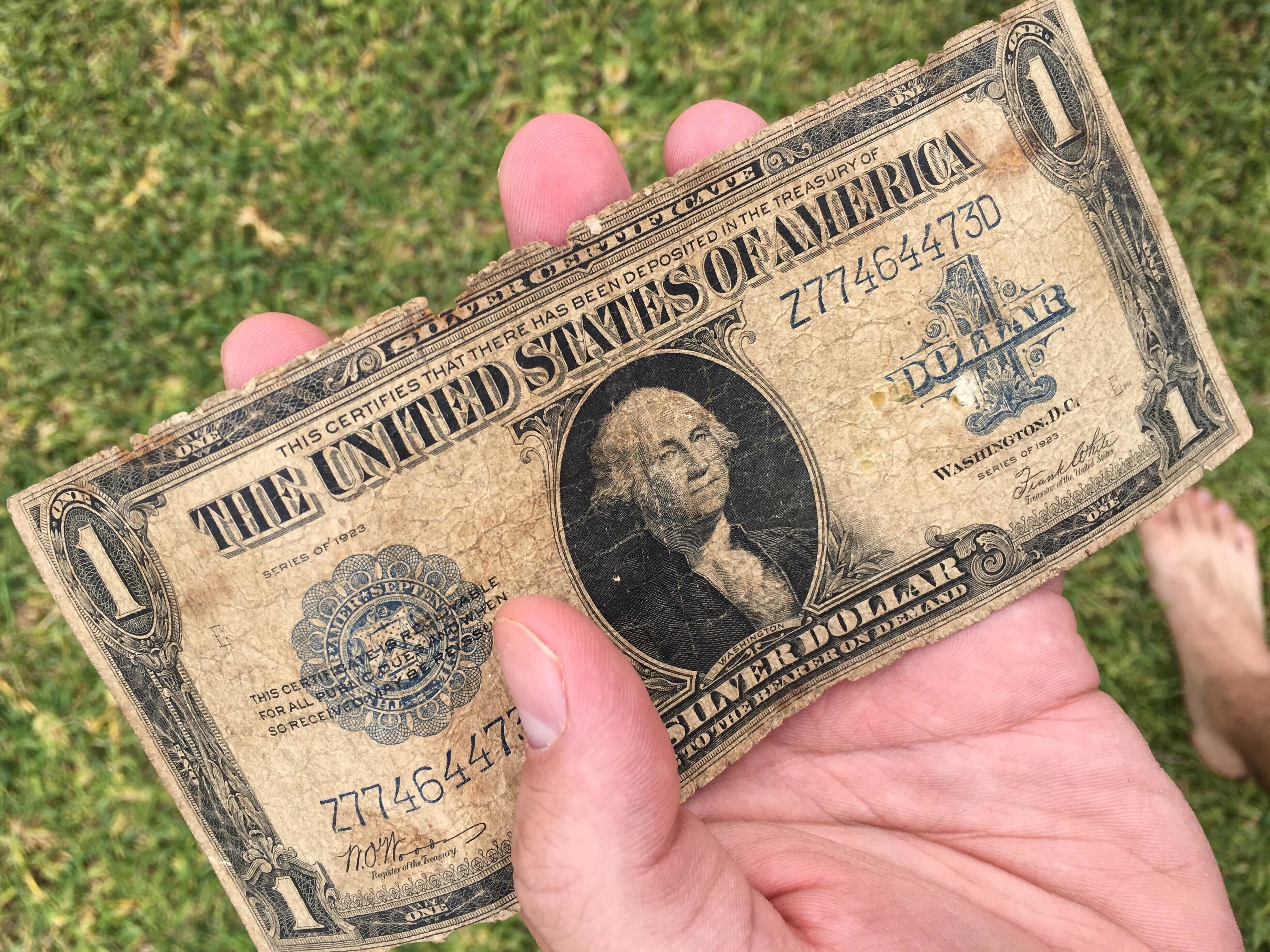 A hand holding an old dollar bill, which says &quot;silver dollar&quot; below the image of George Washington