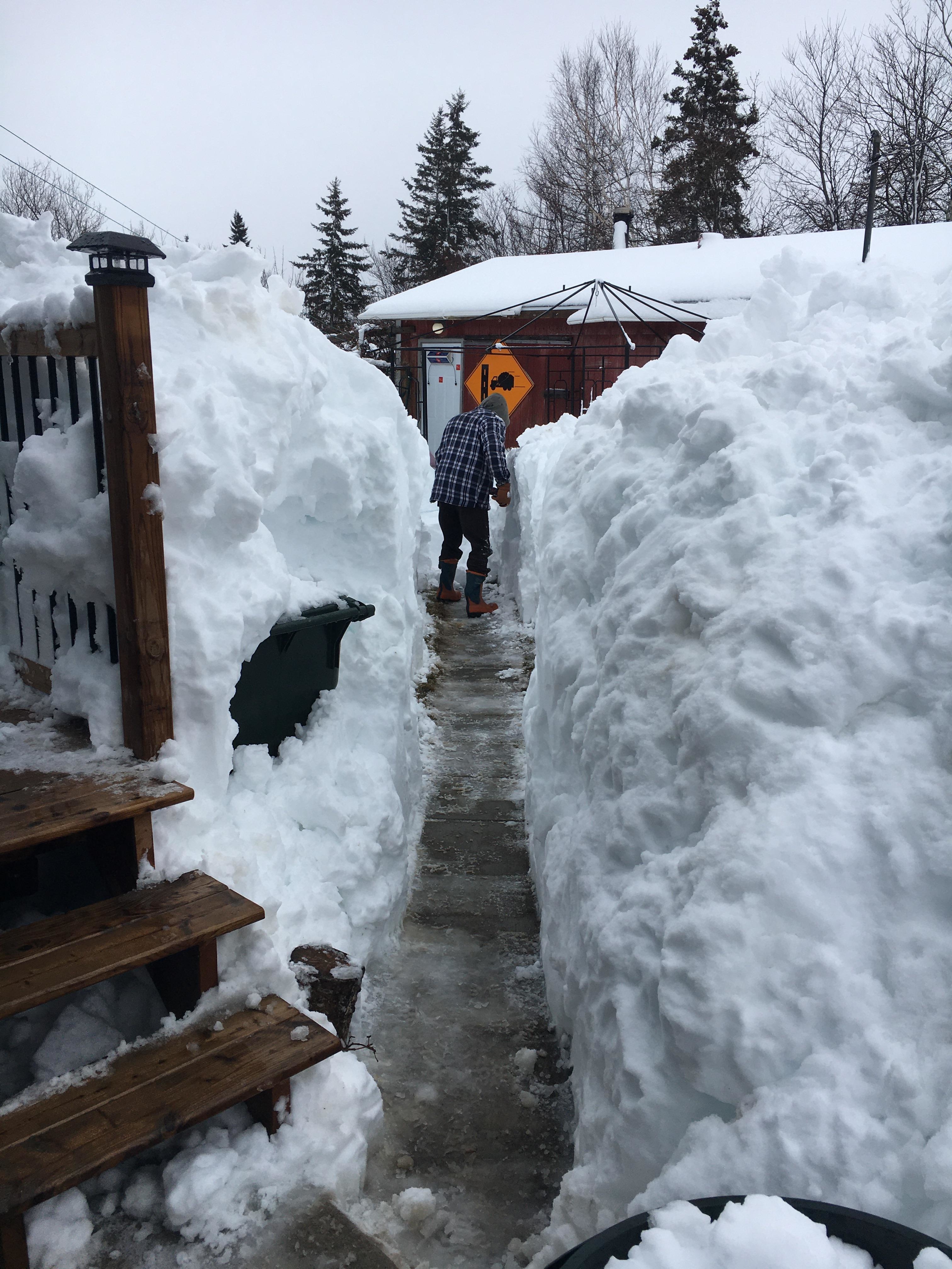 A person making a path with mountains of snow towering above him on either side