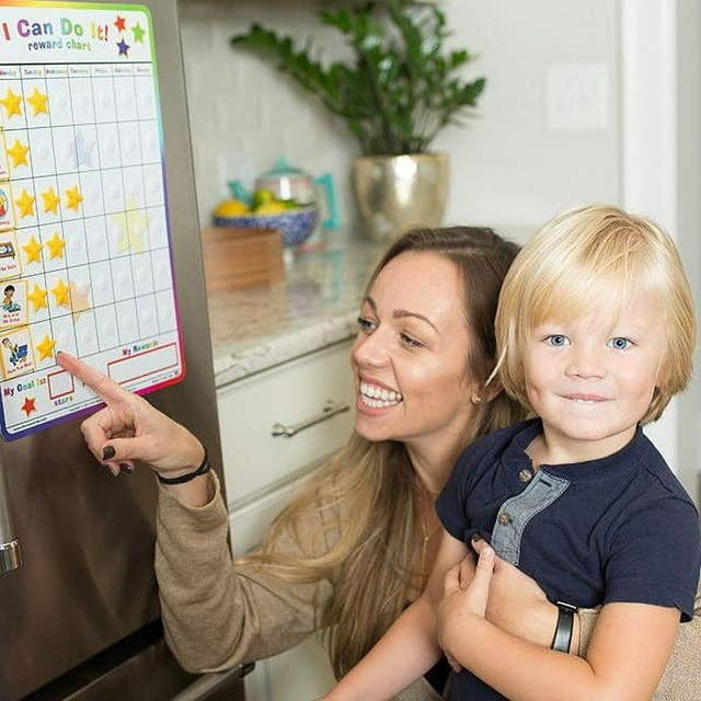 Mom holding kid while pointing at a reward chart
