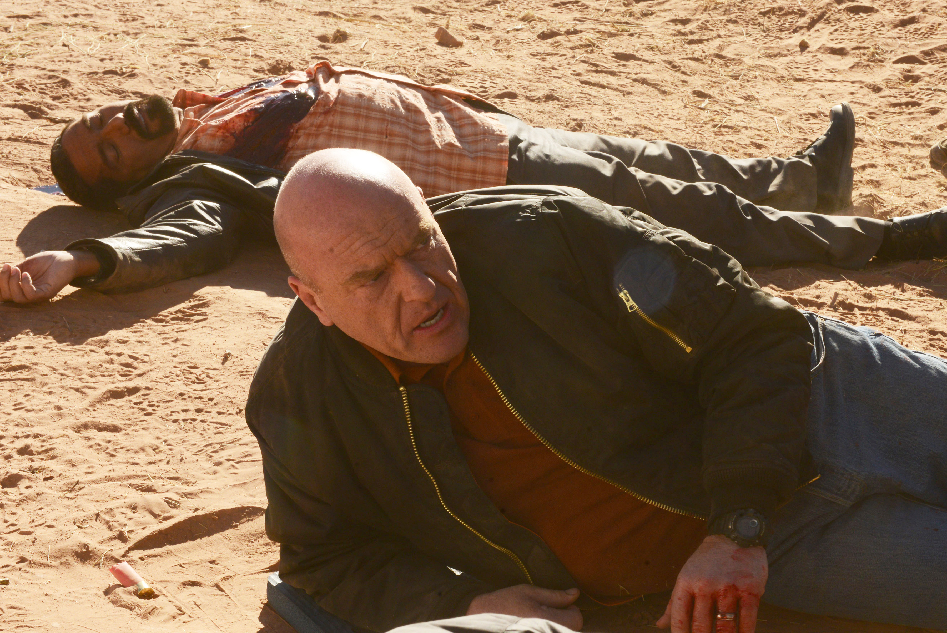 hank with blood on his hands, laying on the desert ground