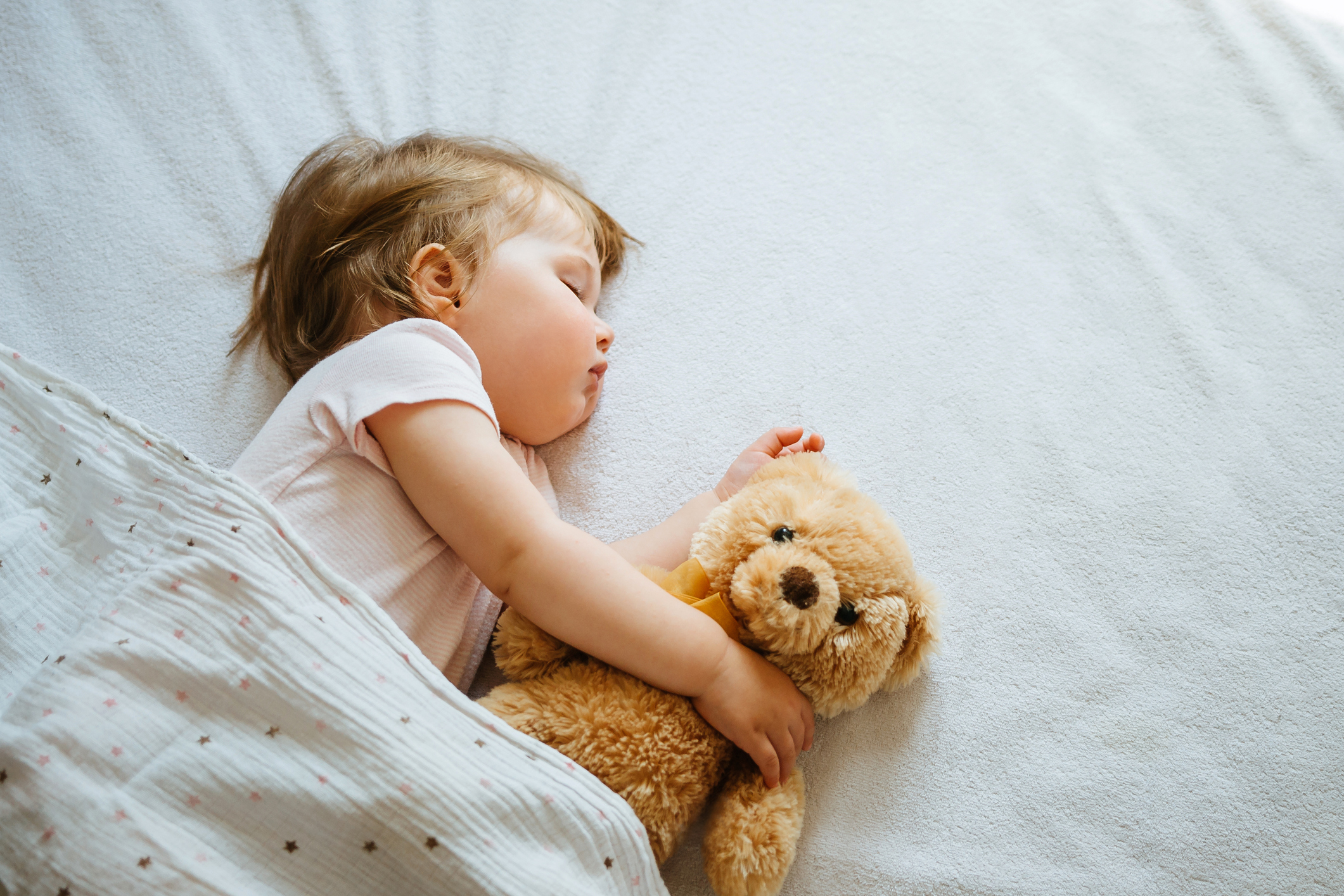 A baby asleep holding a stuffed bear