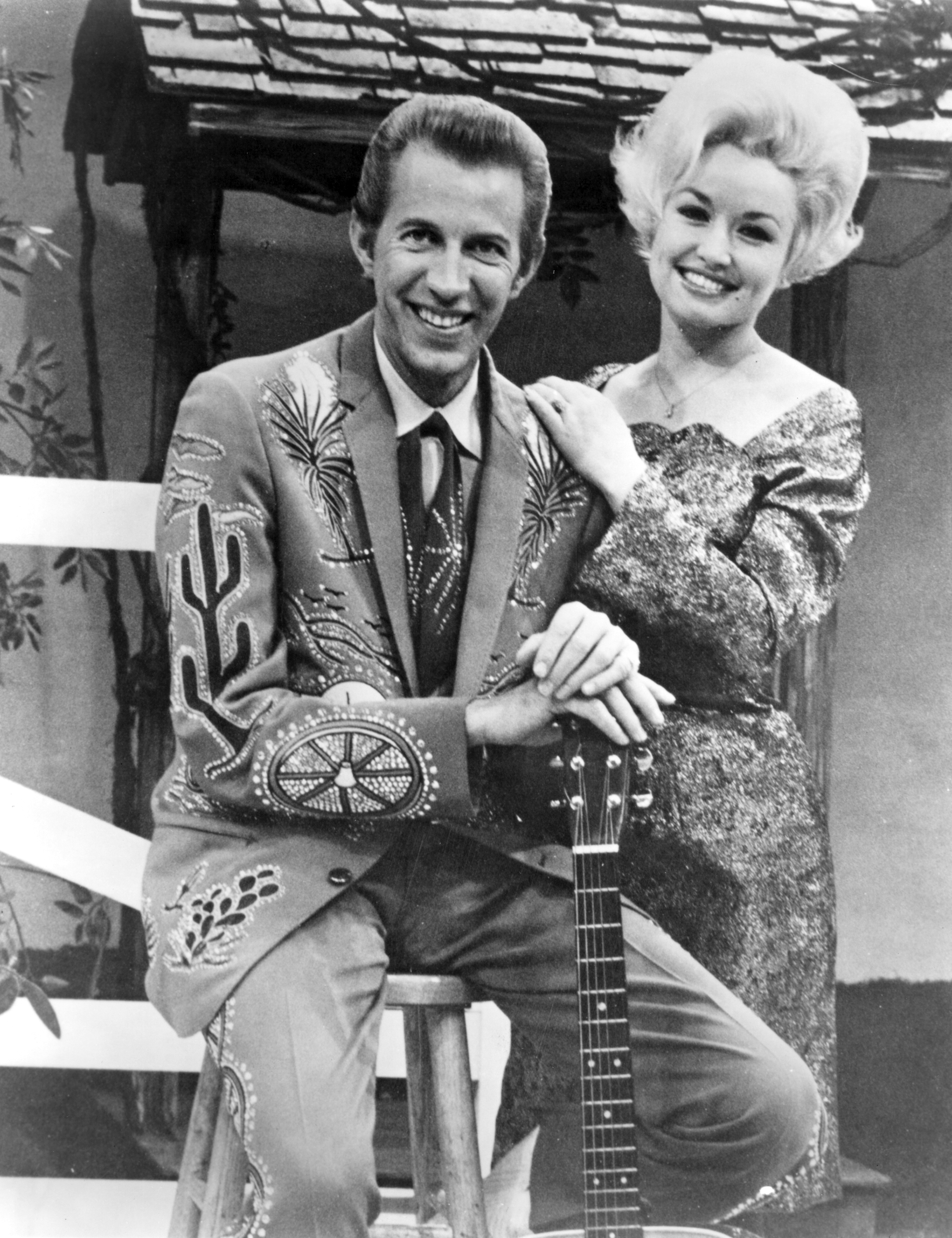 Smiling with a bouffant hairdo next to a man in a spangled outfit