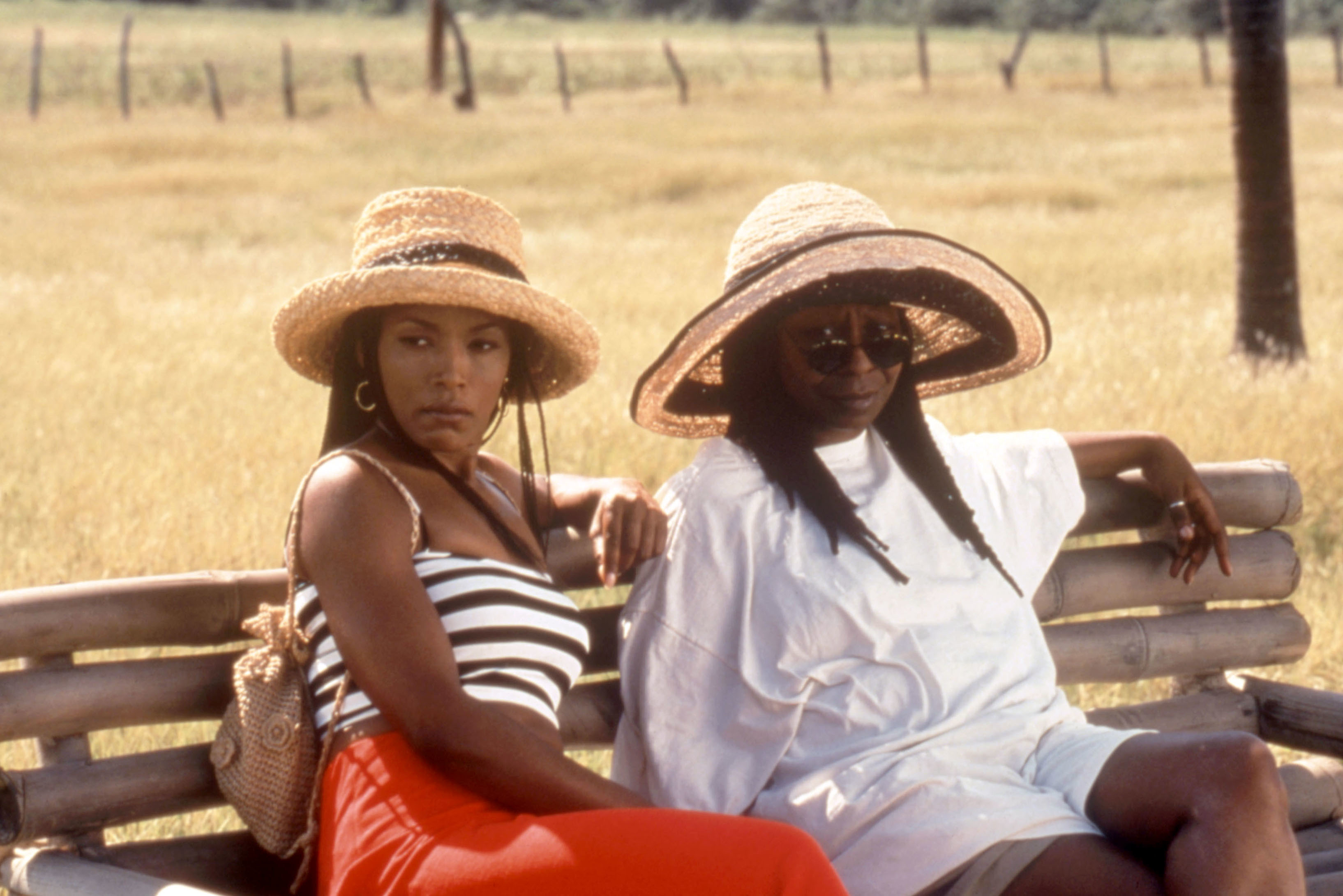 two women wearing sun hats sitting on a bench outside