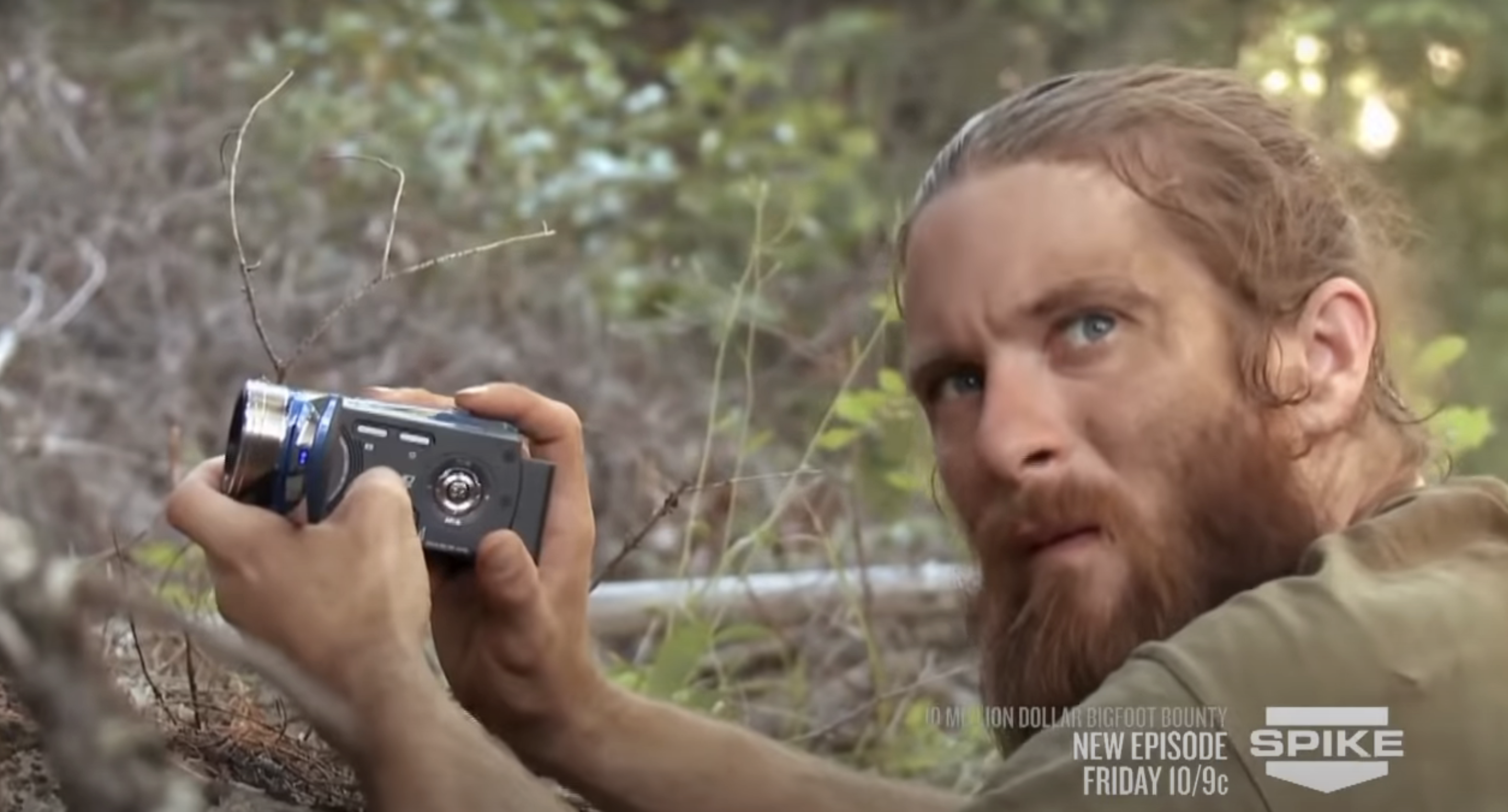 Close=up of a man with a beard outside holding a small camera