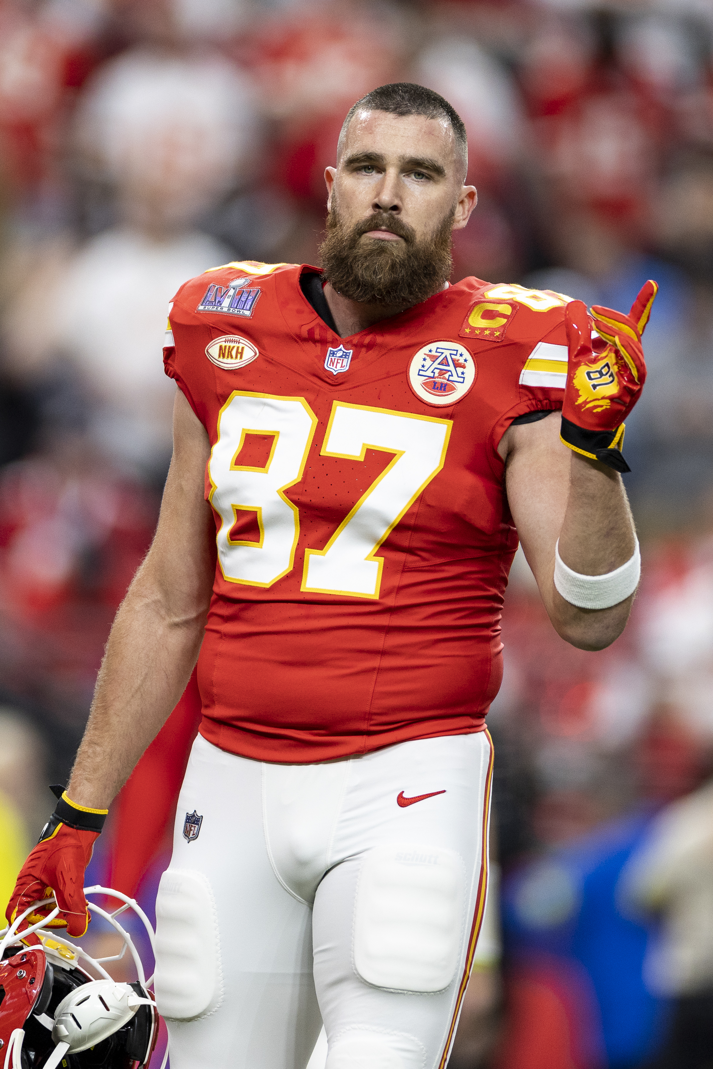 Travis Kelce in football uniform on the field making a hand gesture with one finger up