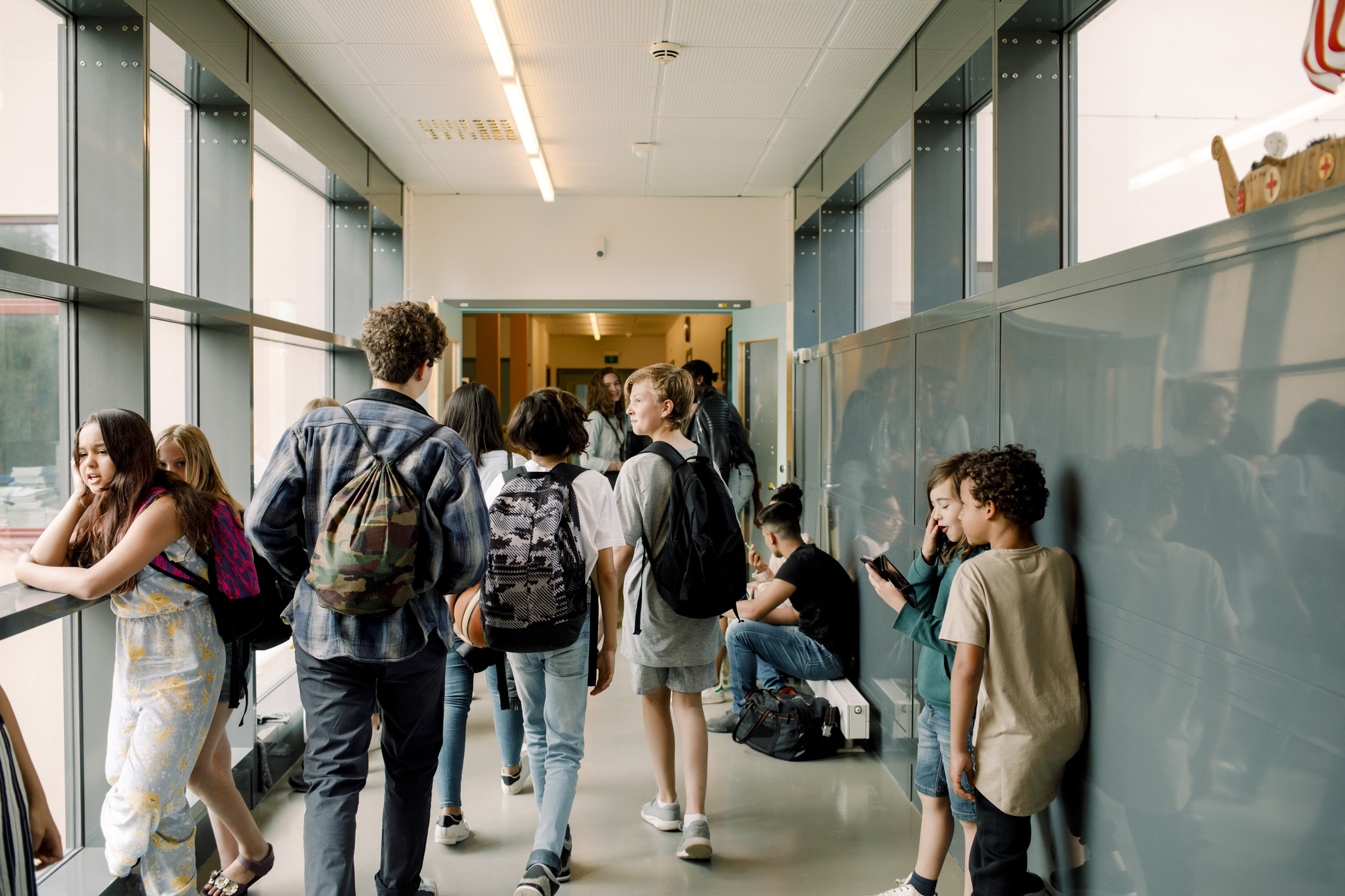 Group of students with backpacks in a school hallway, interacting by lockers