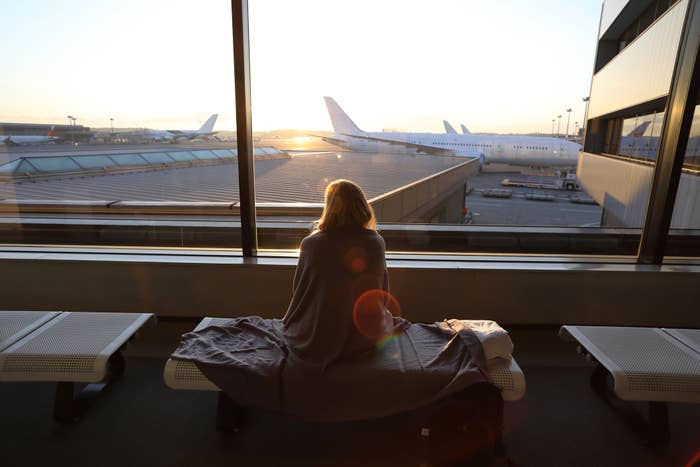 Person sitting in an airport lounge, looking out at planes during sunrise, embodying a moment of calm travel
