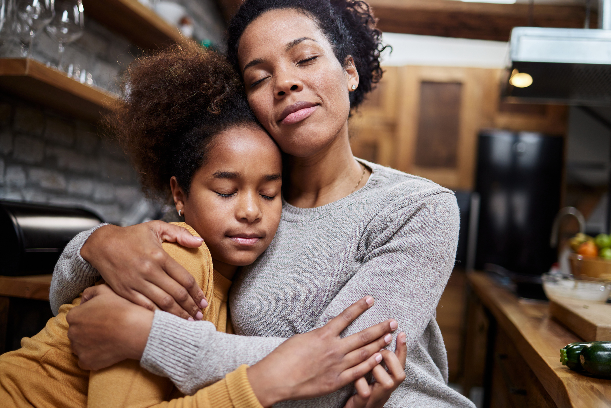 Mom and daughter embracing each other in a kitchen setting, eyes closed, showing a moment of affection