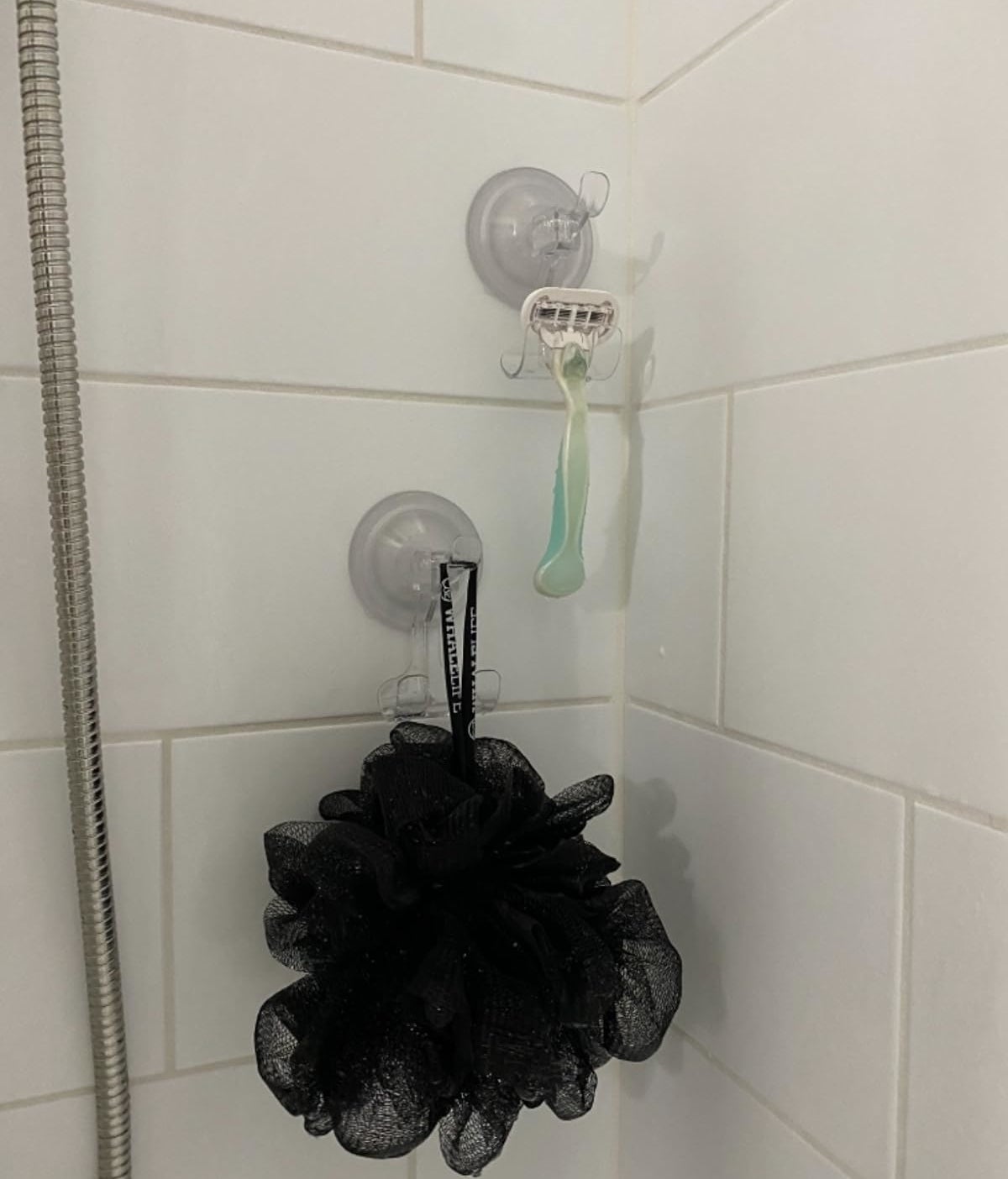 Reviewer&#x27;s shower wall with suction hooks holding a razor and loofah