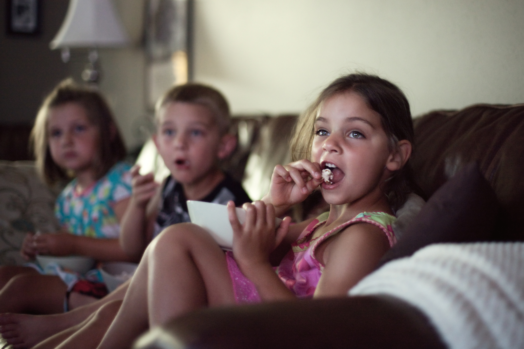 Three children watching TV, one eating, expressing focus and surprise