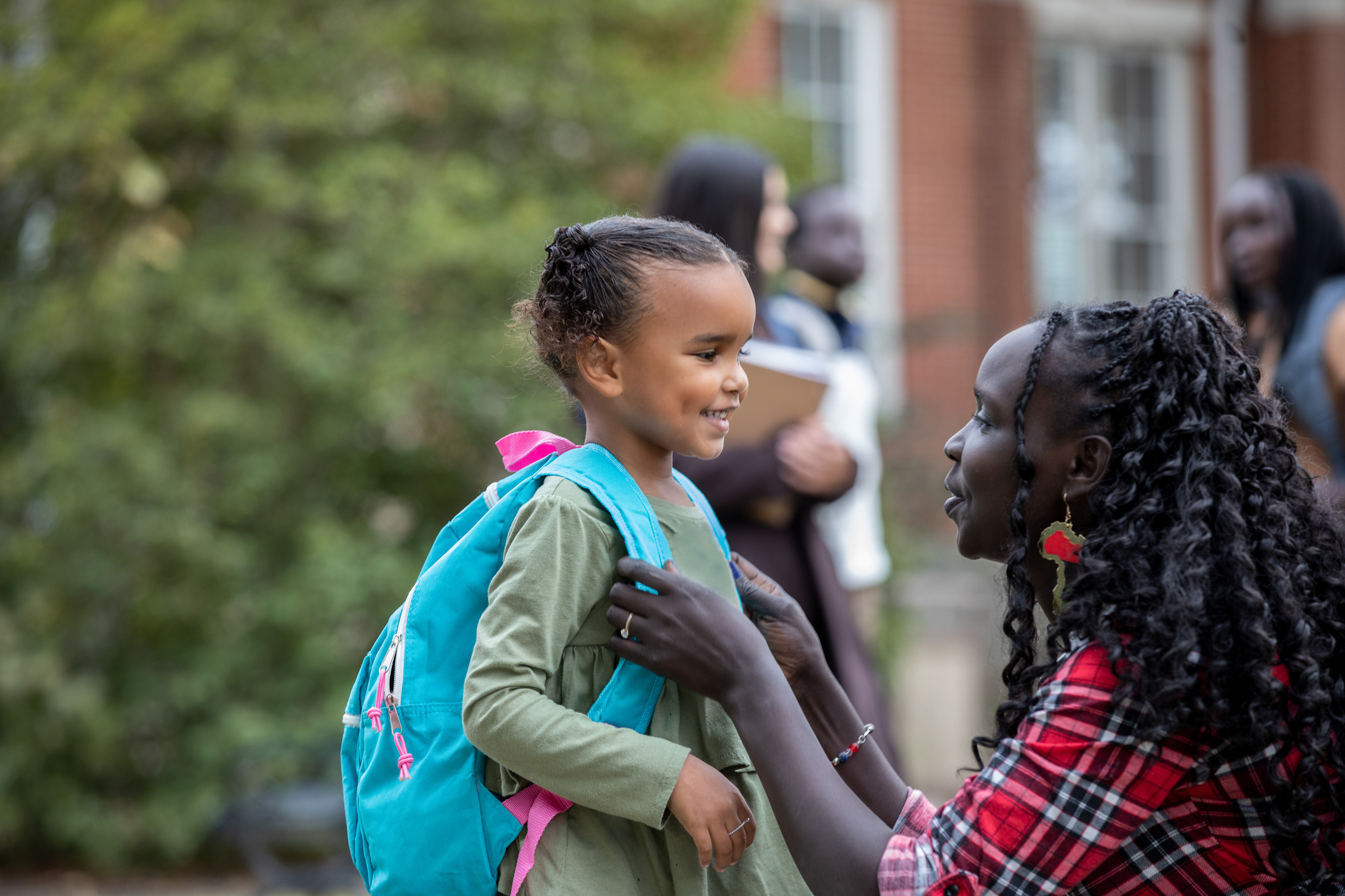 Mother lovingly looks at young daughter with backpack outside school