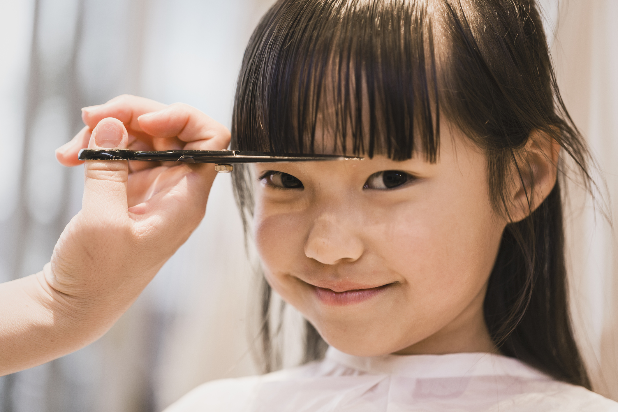 Child smiling during a haircut, bangs being trimmed