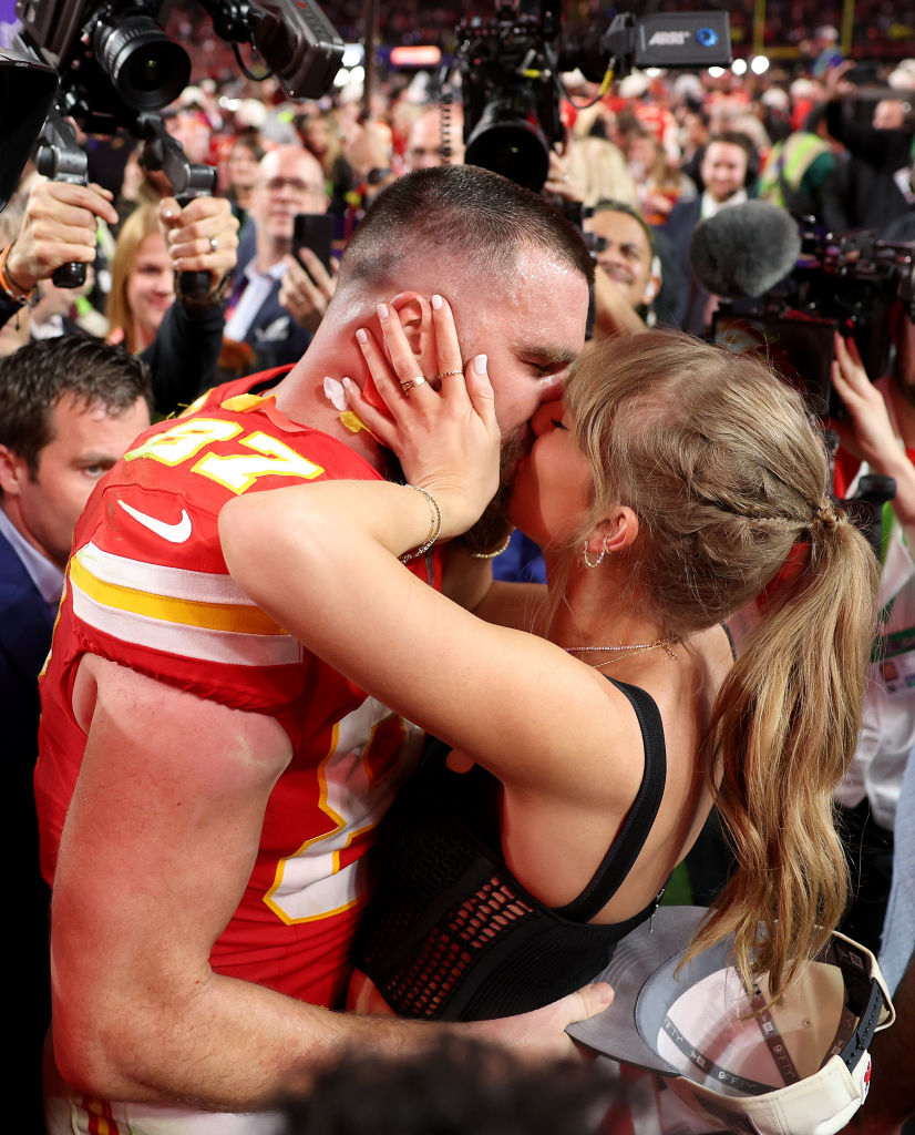Travis Kelce being kissed by Taylor amidst celebrating fans and cameras after a game