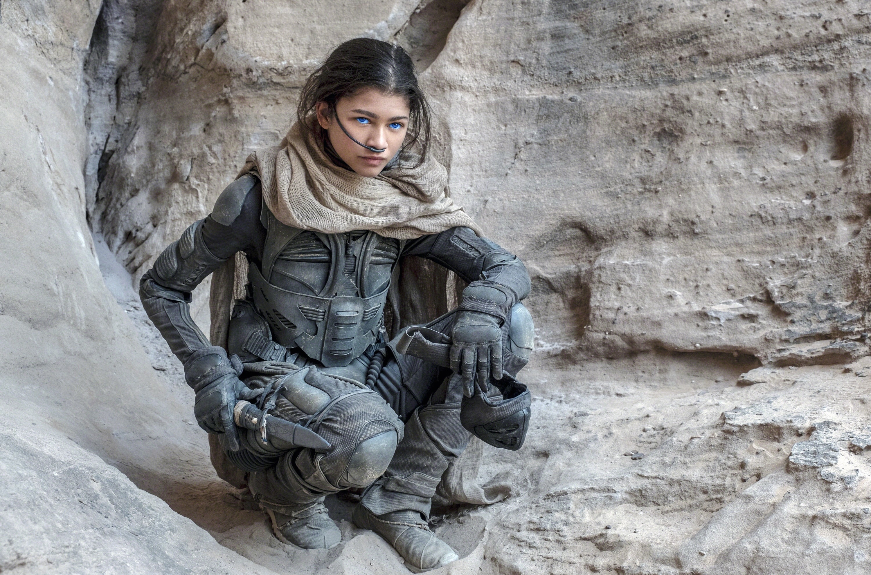 Zendaya in Dune sitting against a rock backdrop, looking thoughtful