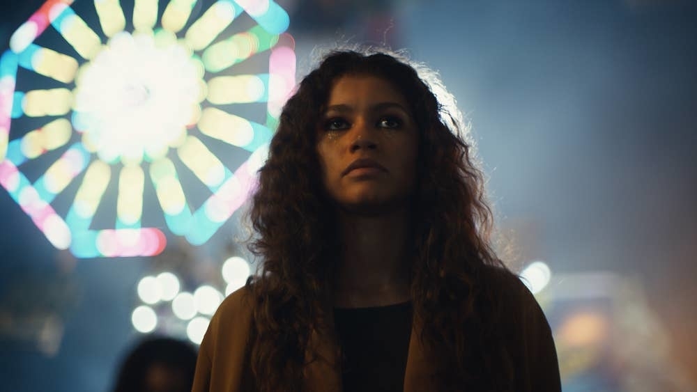 her character in front of blurred ferris wheel at night. She has a serious expression
