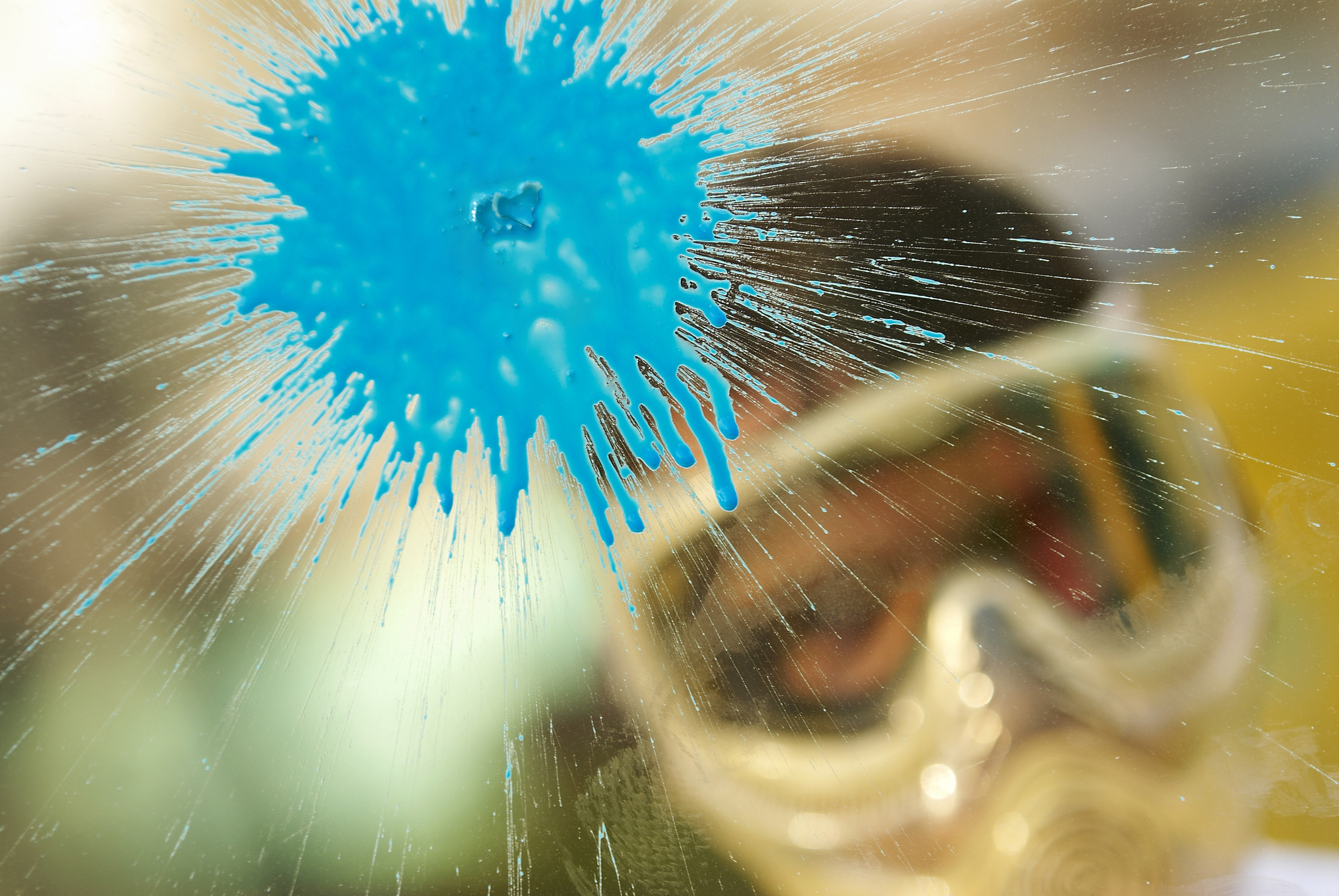 Paint splash on glass with person in protective gear visible through smear
