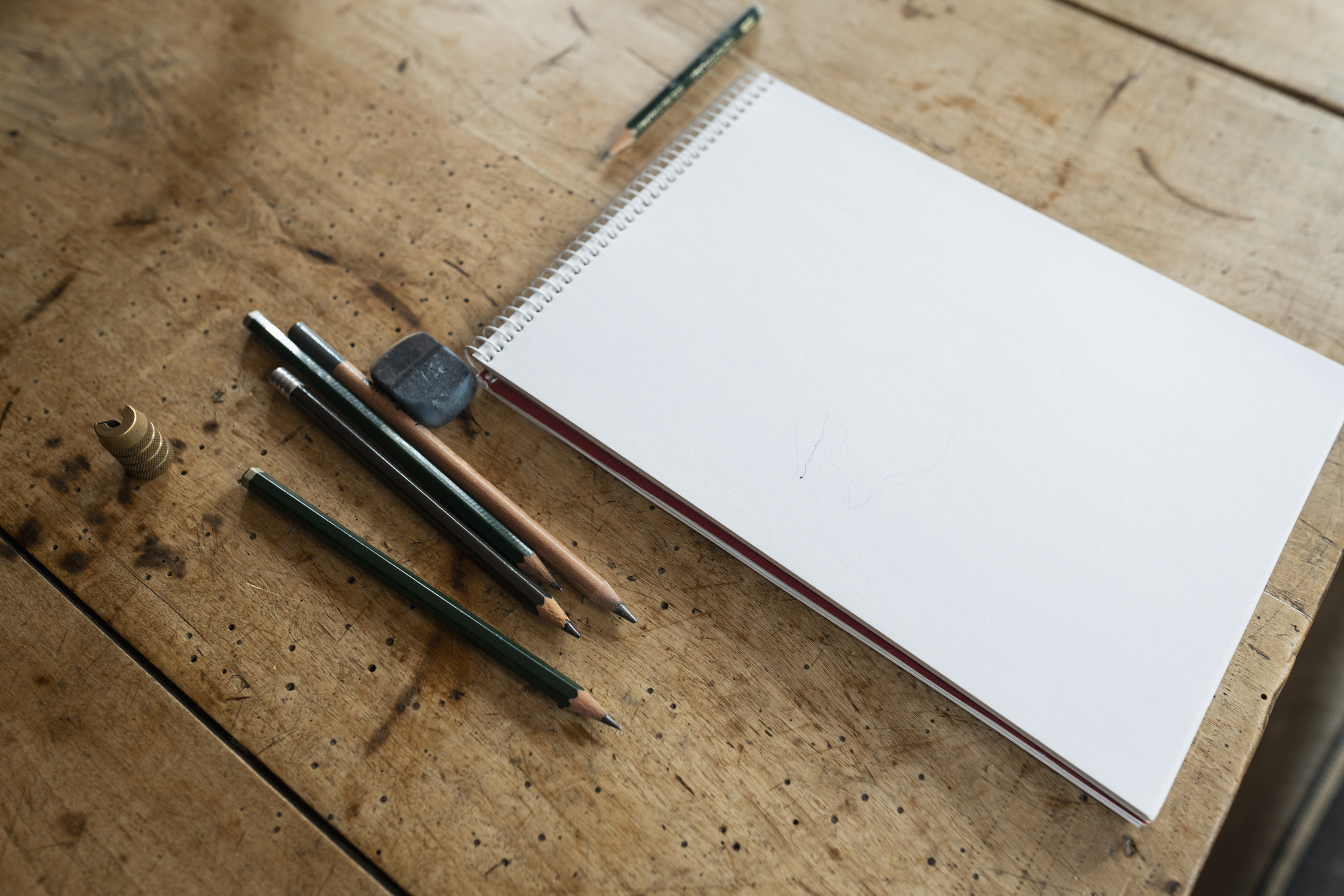 A sketchbook with blank pages next to pencils and an eraser on a wooden surface