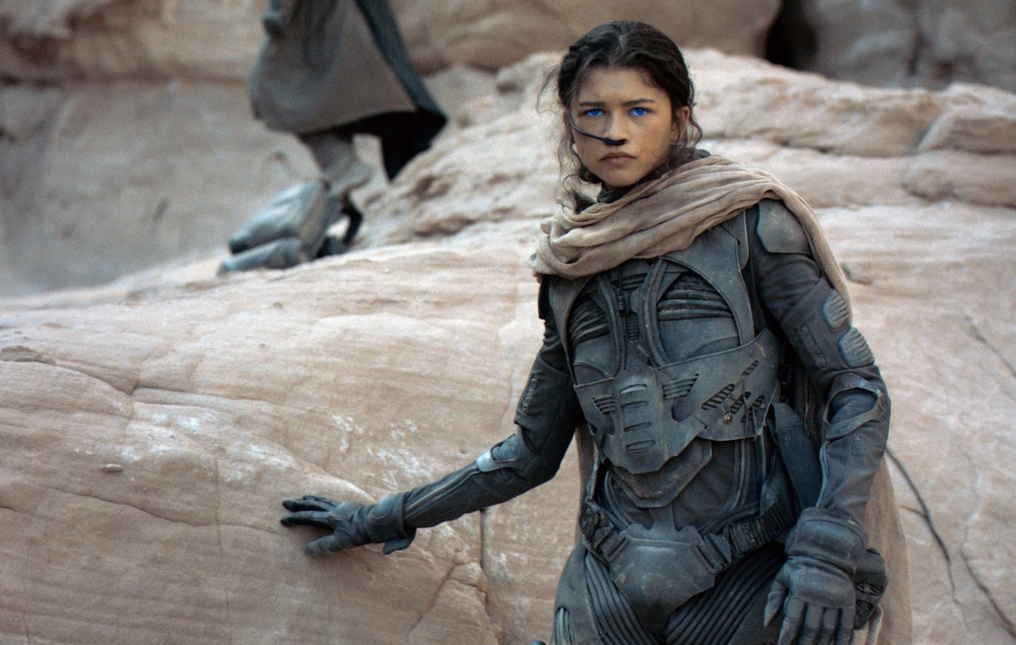 Zendaya in futuristic armor crouches on rocky terrain in a scene from a movie