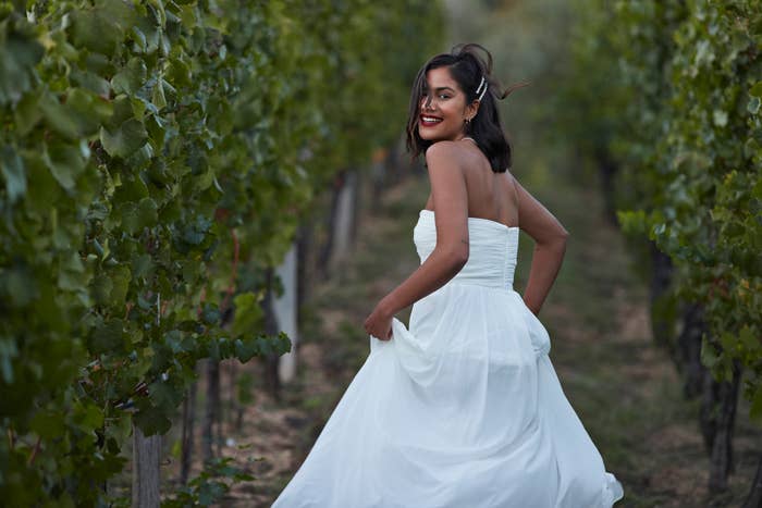 Woman in a white strapless wedding gown smiling over her shoulder in a vineyard