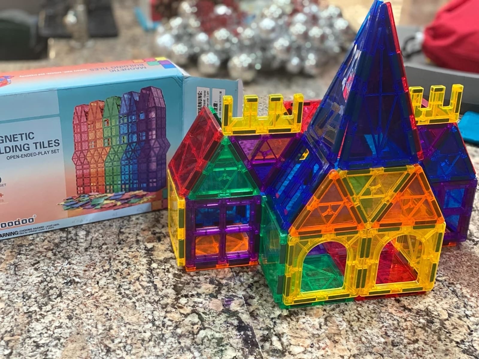 A set of colorful magnetic building tiles assembled into a house-like structure, with the product box in the background